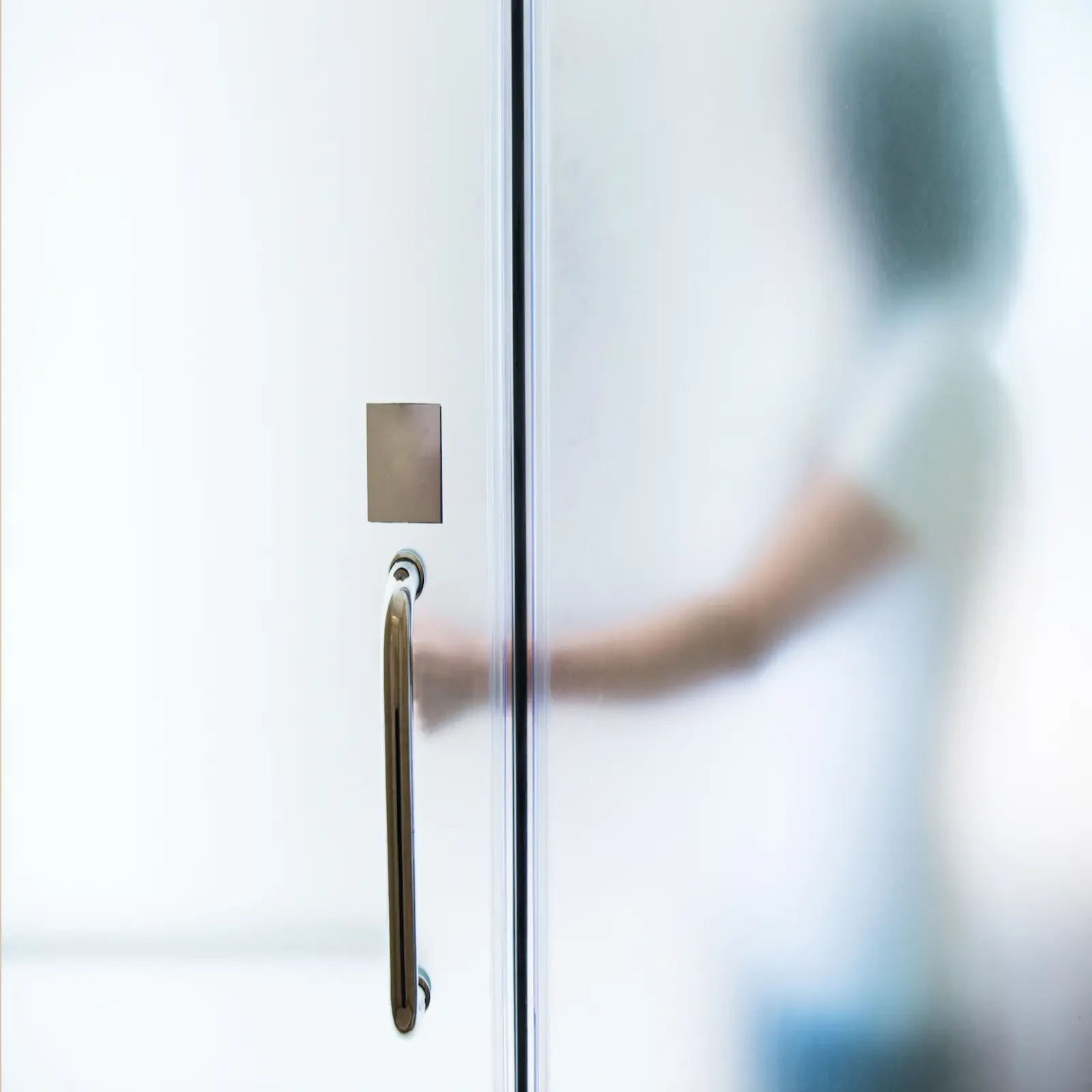 Une porte en verre opaque avec une poignée en métal et une silhouette floue d'une personne derrière