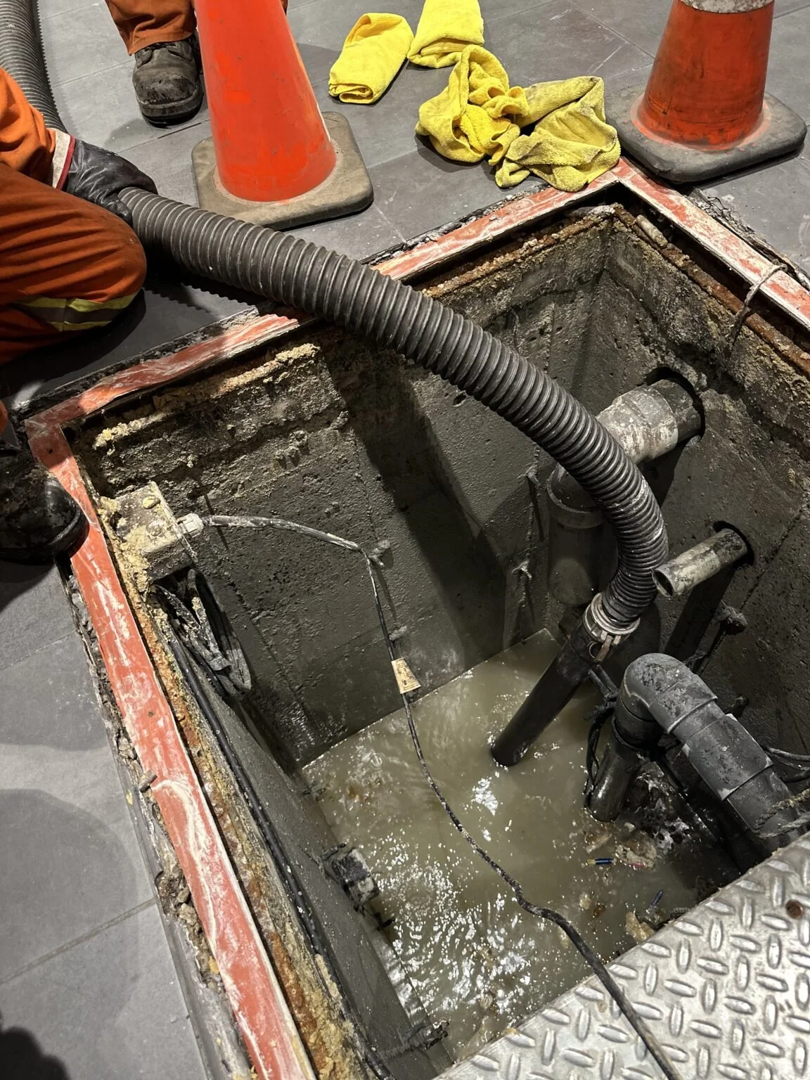Workers repairing or inspecting underground water or sewer pipes with open trench and visible water.