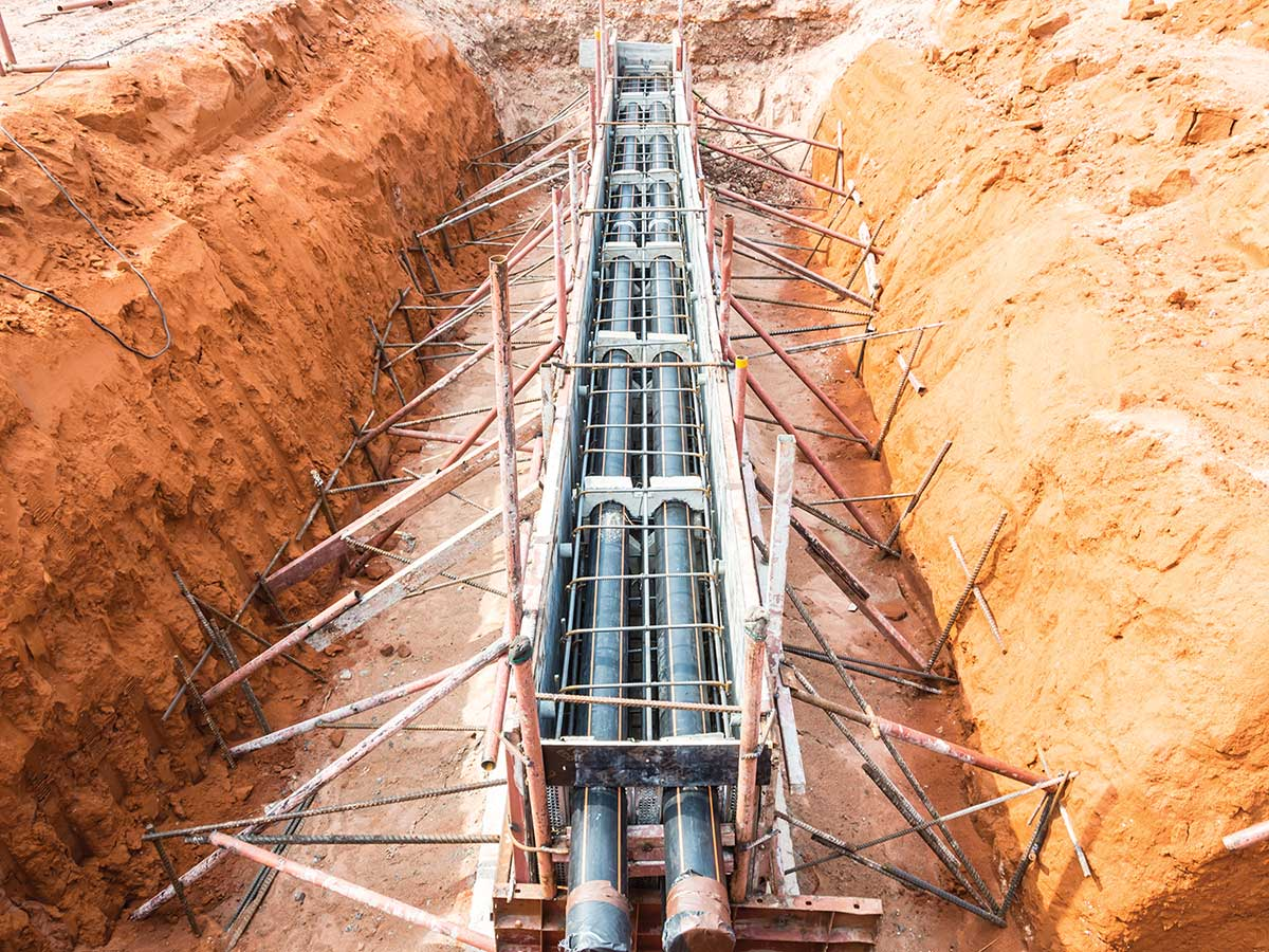 Construction site with large pipes and scaffolding in a deep trench with orange soil.