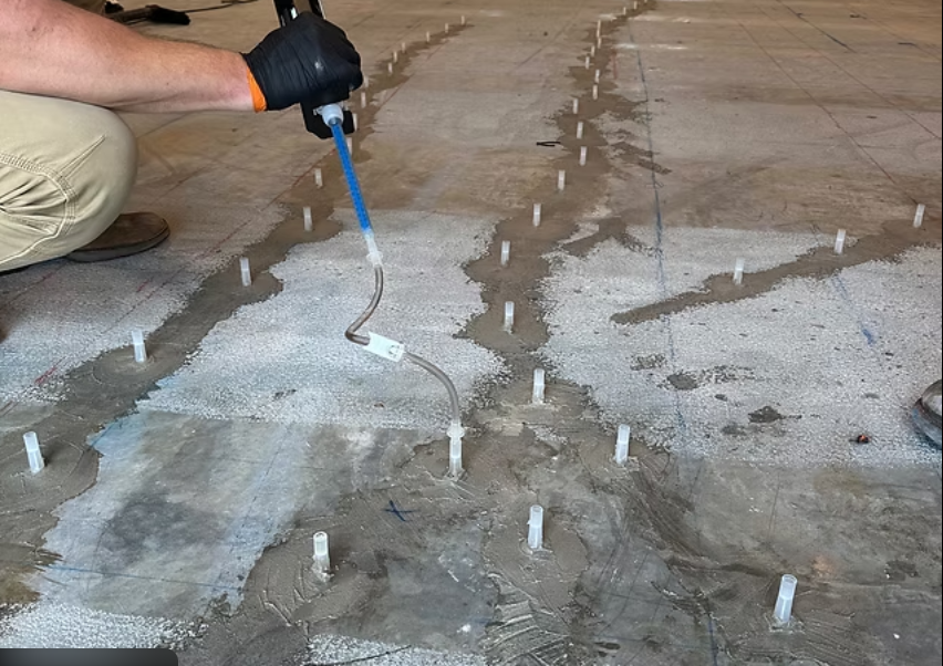 Worker using a tool to inject liquid into concrete with plastic form stakes for leveling.