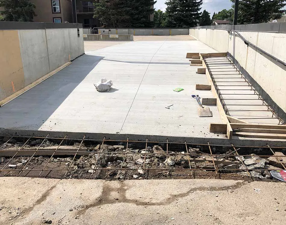 Construction site showing the installation of concrete on a rooftop parking area with rebar and wooden forms for expansion joints.