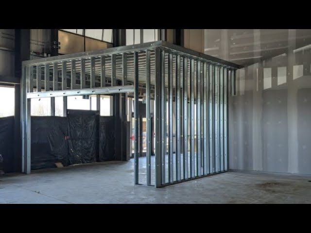 Construction site with metal framing for walls and a raised ceiling, partially enclosed.