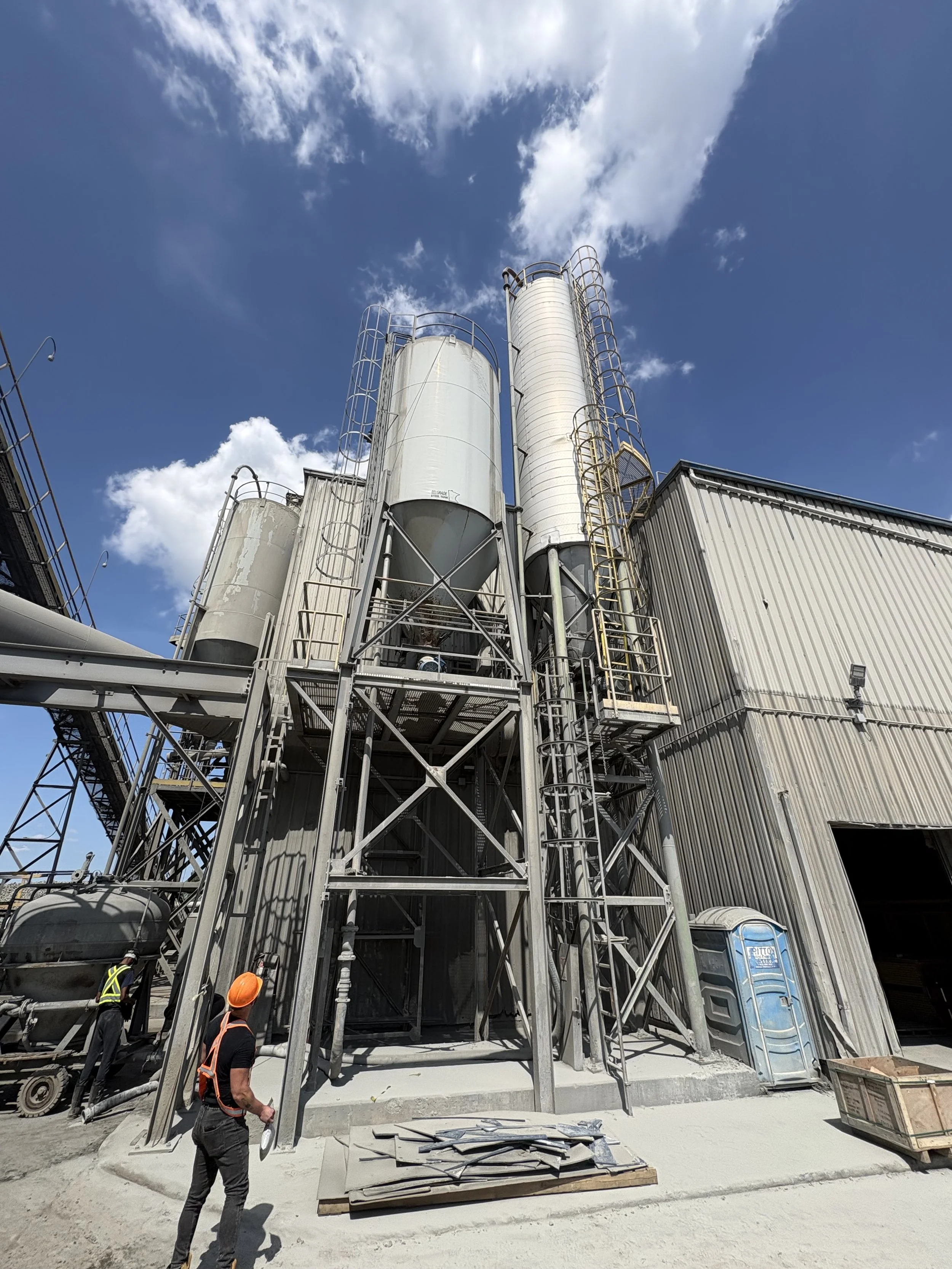 Construction site with large metal silos and workers in hard hats.