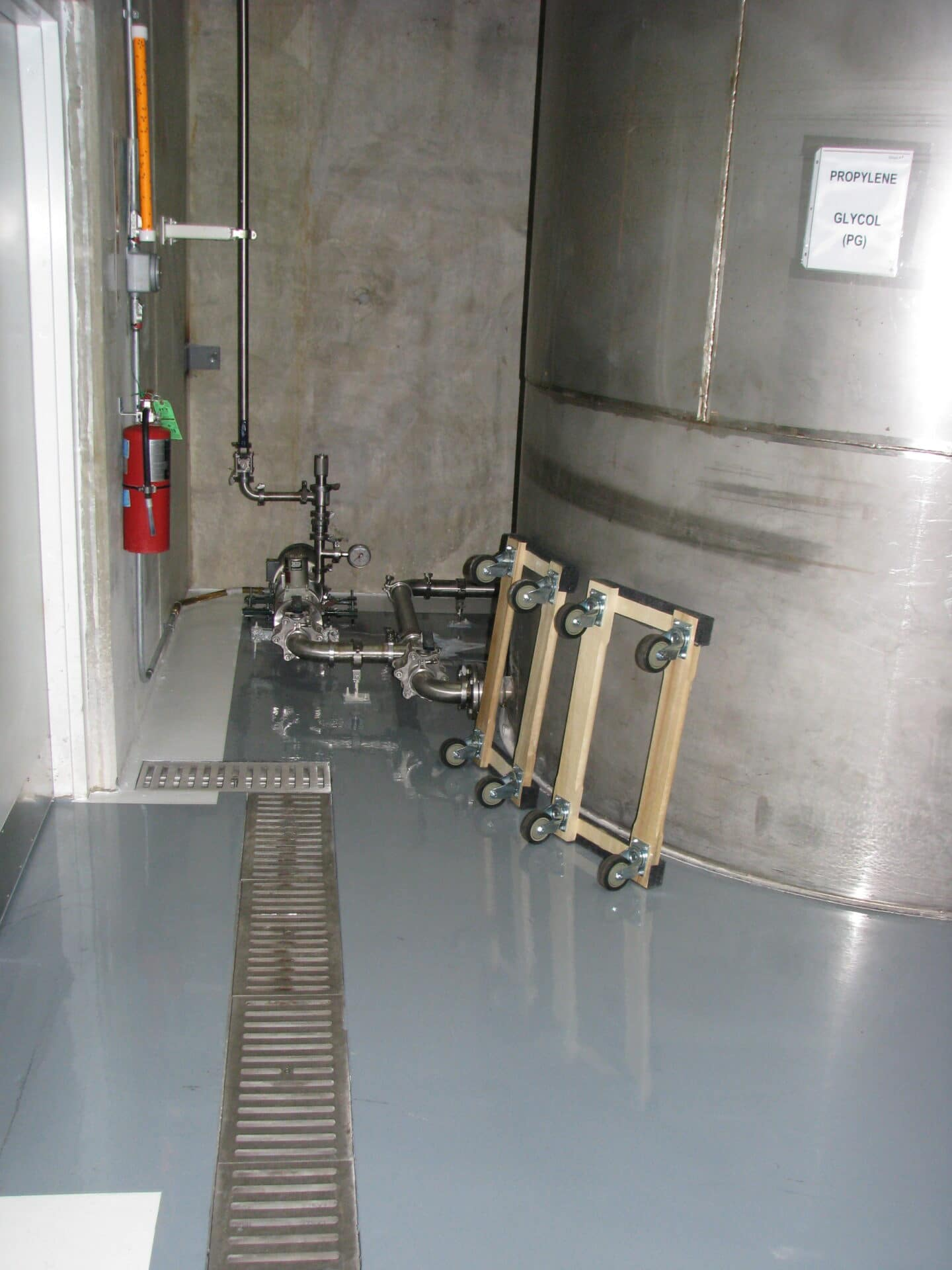 Indoor industrial room with pipes and valves, a fire extinguisher, a grate in the floor, and a sign that reads 'Propylene Glycol (PG).'