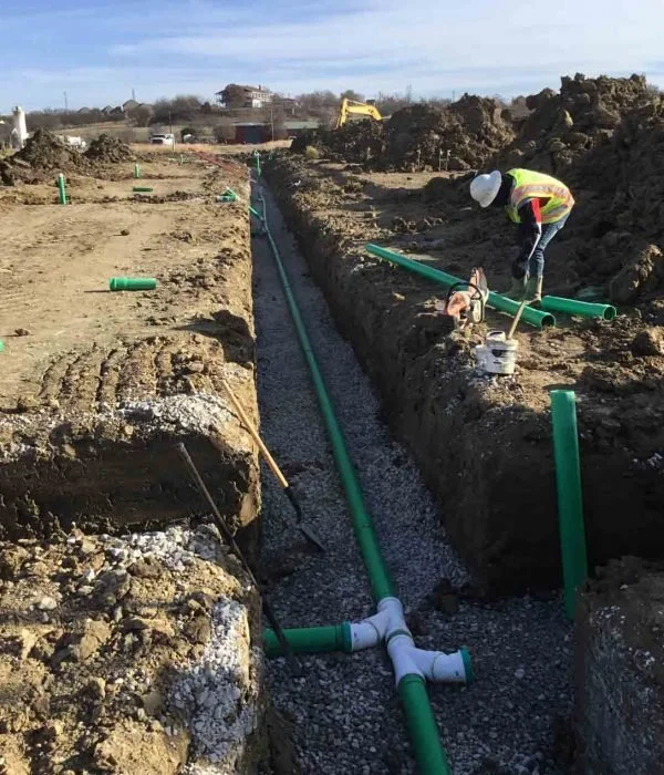 Construction worker installing green pipes in a trench on a construction site.