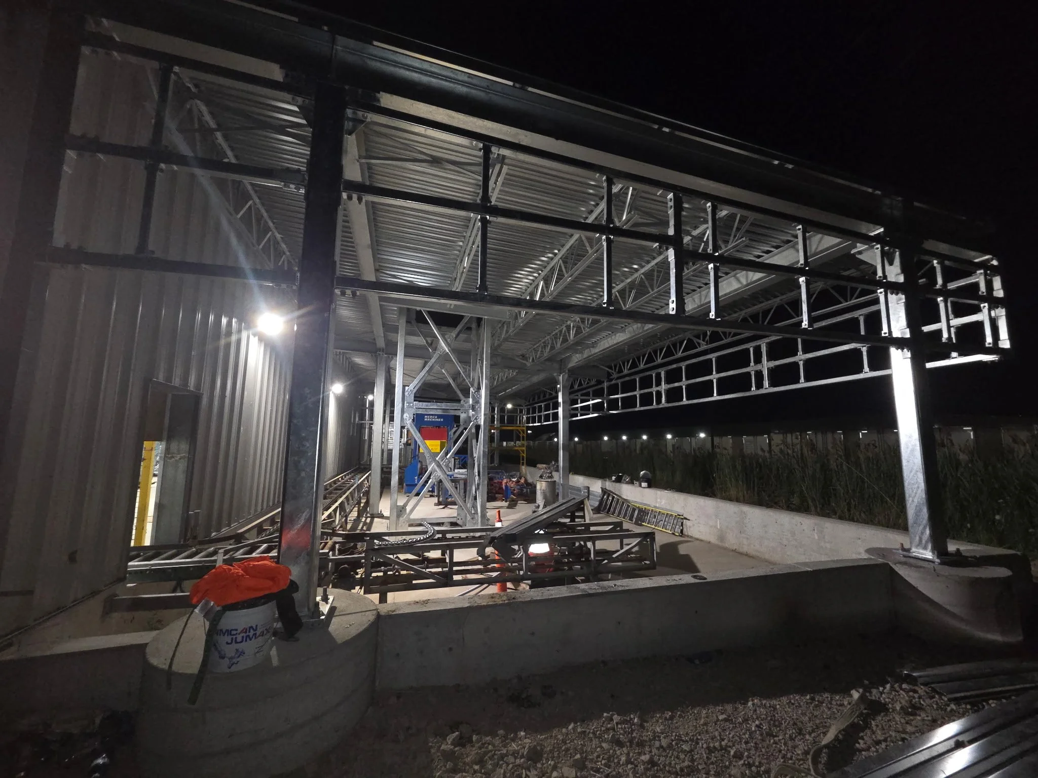 Construction site at night with metallic frame structure and scaffolding under development, illuminated by outdoor lights.