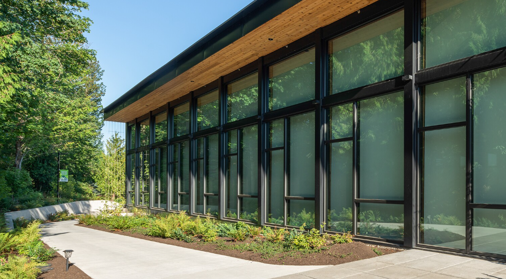 Modern building with large glass windows and a landscaped pathway in a green outdoor setting.