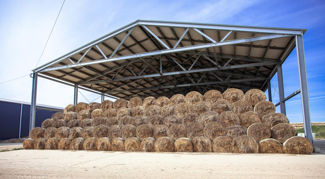 Stack of hay bales in a metal shelter on a farm.