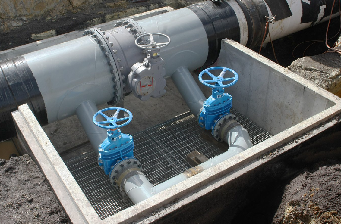 Large pipeline with two blue valves inside a concrete basin at a construction site.