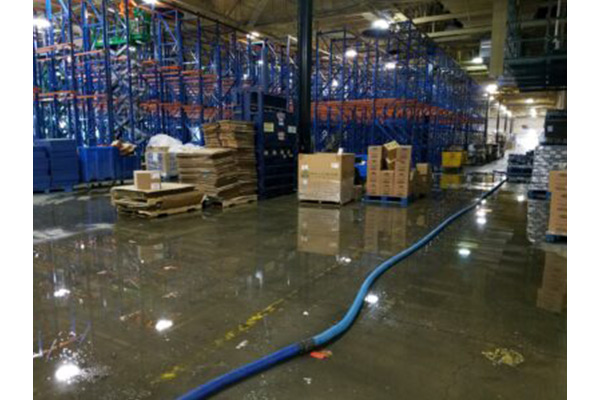 Warehouse with storage racks, boxes, and a hose on the wet floor.