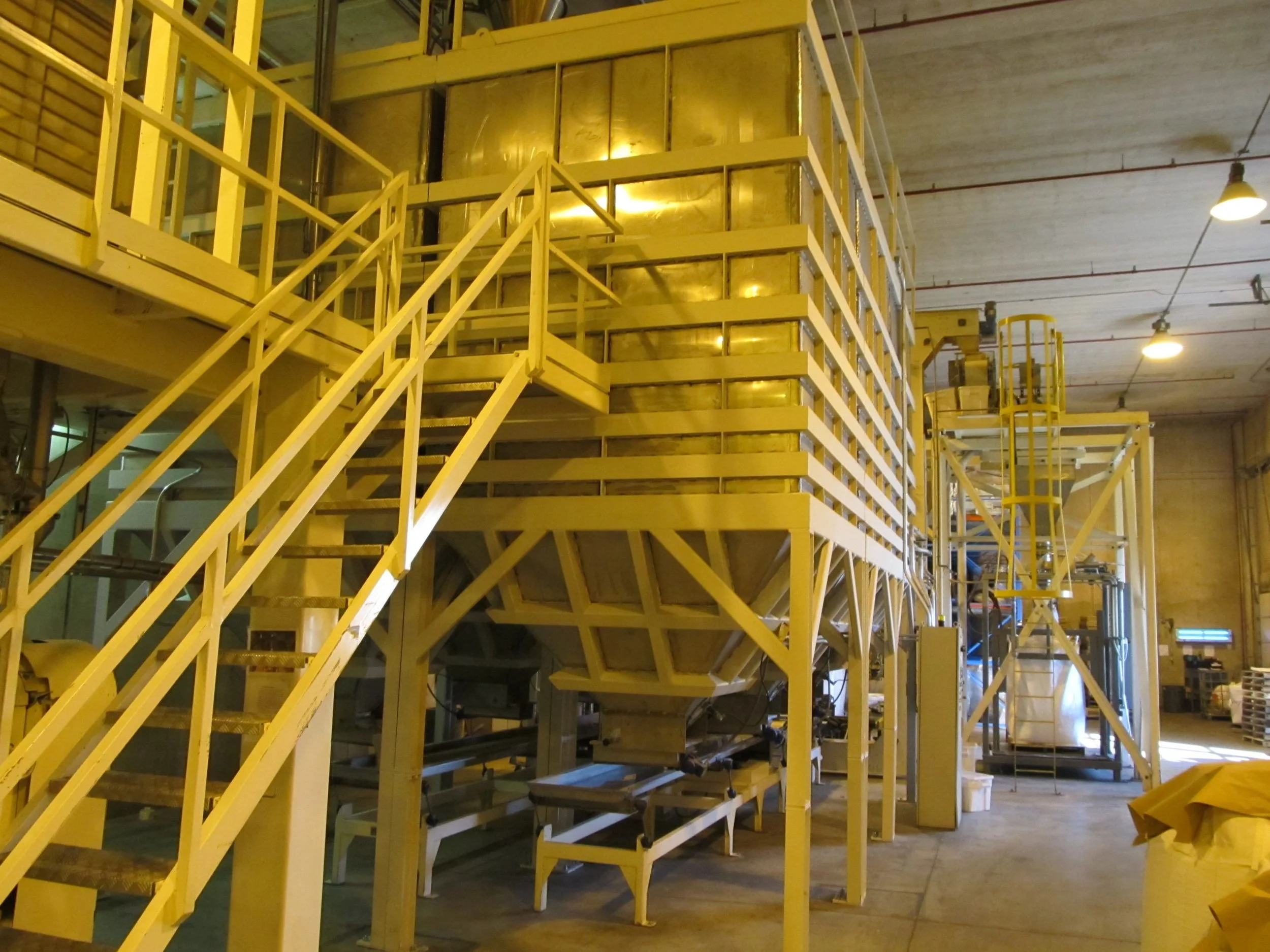 Industrial facility with yellow stairs and metal structures, machinery, and control panels in a warehouse or factory setting.