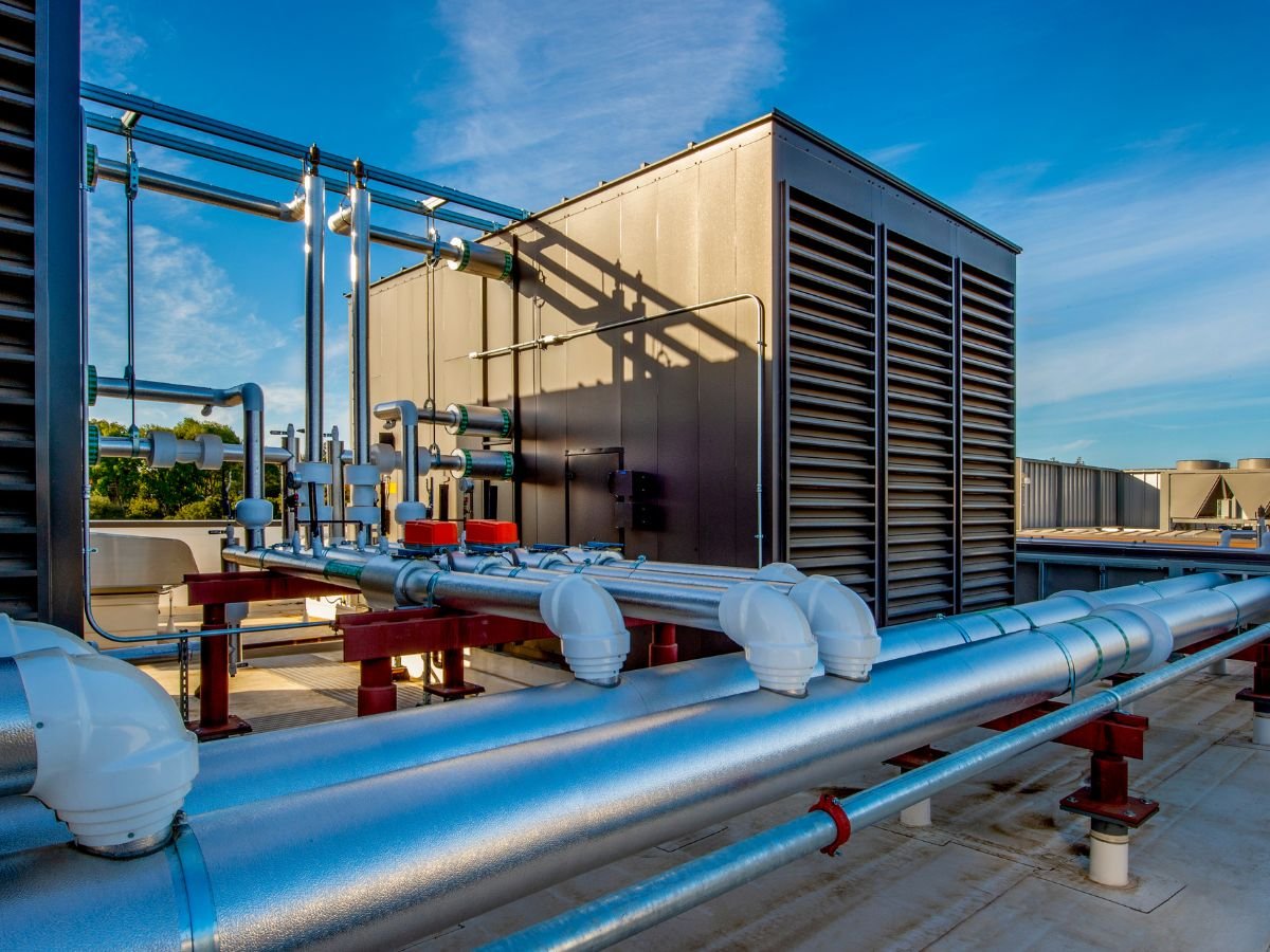 Rooftop HVAC unit with metal ventilation pipes and ducts against a blue sky.