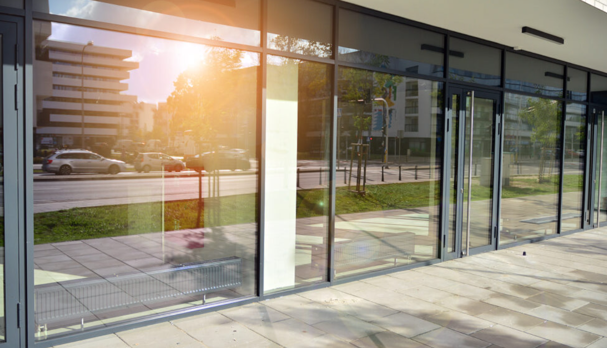 Modern building with large glass windows reflecting the street, cars, trees, and buildings outside during sunset.