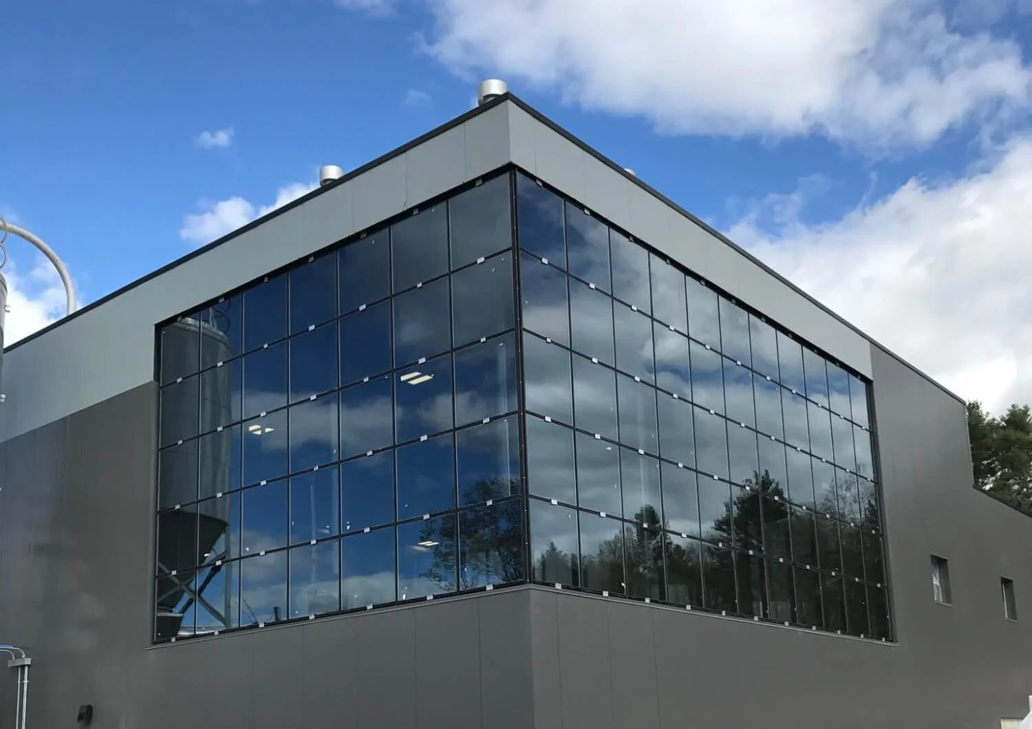 Modern building with large glass windows reflecting the cloudy sky and trees.