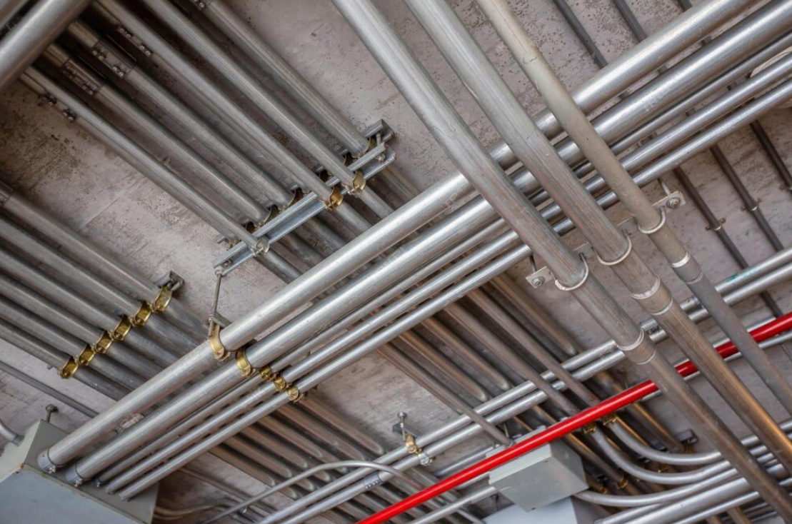 Network of metal pipes and conduits mounted on a ceiling.
