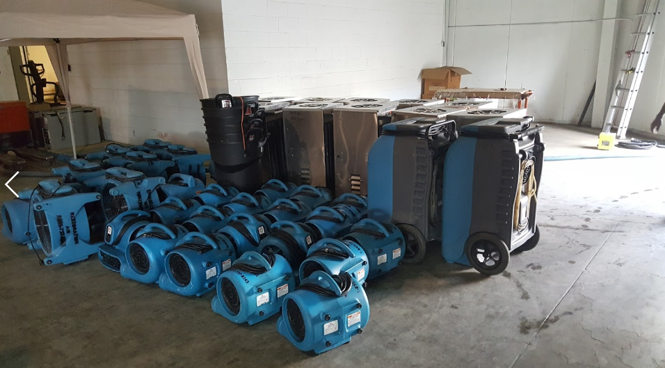 Collection of blue and black portable industrial air movers or fans in a warehouse or storage area.