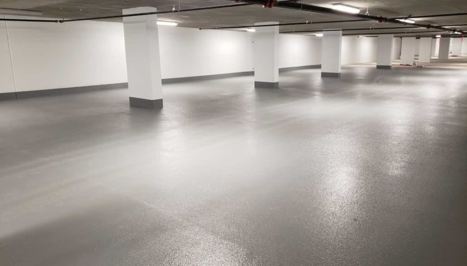 Empty, well-lit underground parking garage with white walls, gray floor, and support columns.