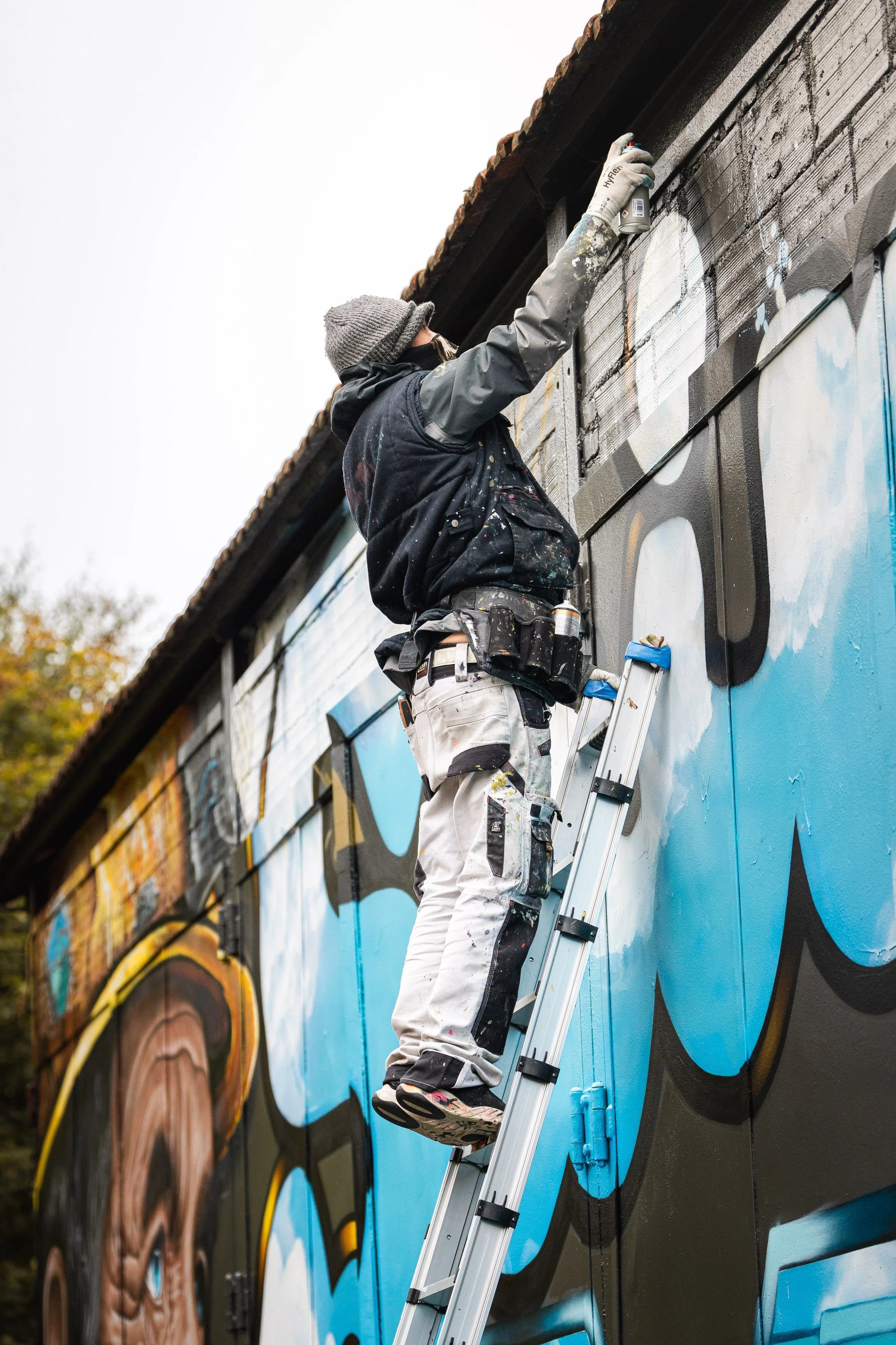 Graffeur sur une échelle peignant une fresque
