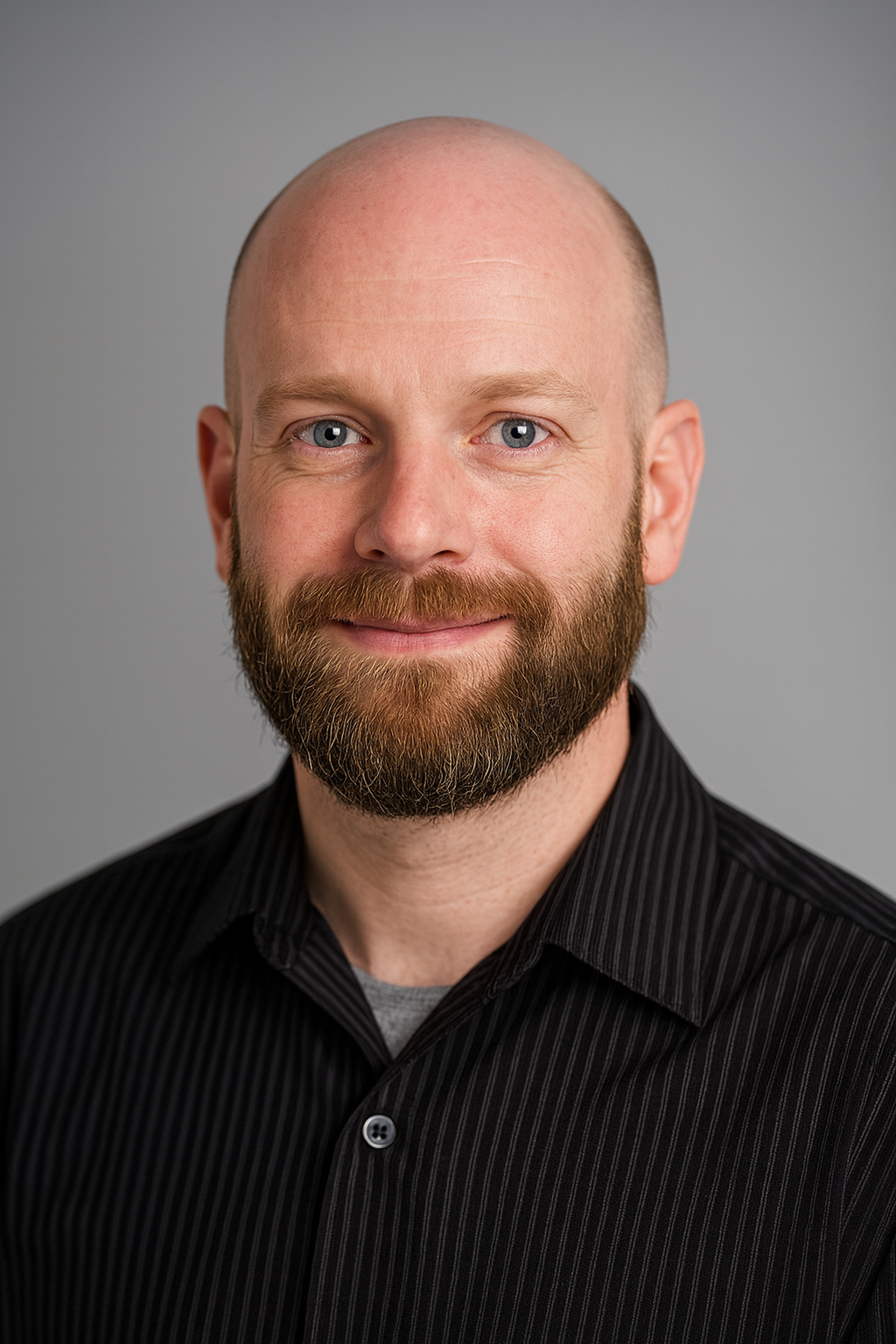 Headshot of a smiling man with a bald head, blue eyes, and a full beard, wearing a black pinstripe shirt against a gray background.