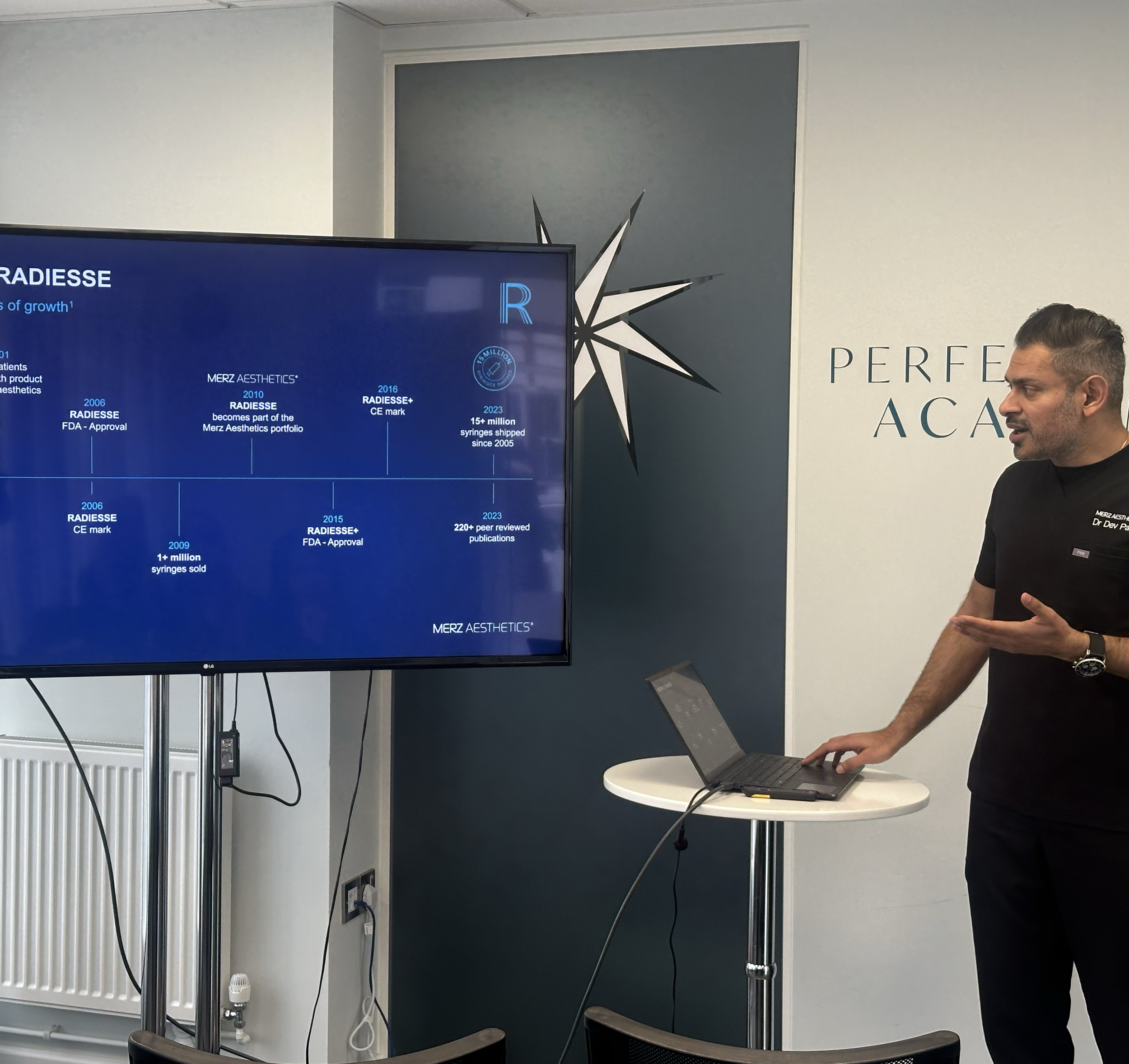 A man standing in front of a presentation screen with a timeline about Radiesse, a cosmetic product, with a partial view of a conference or classroom setting.