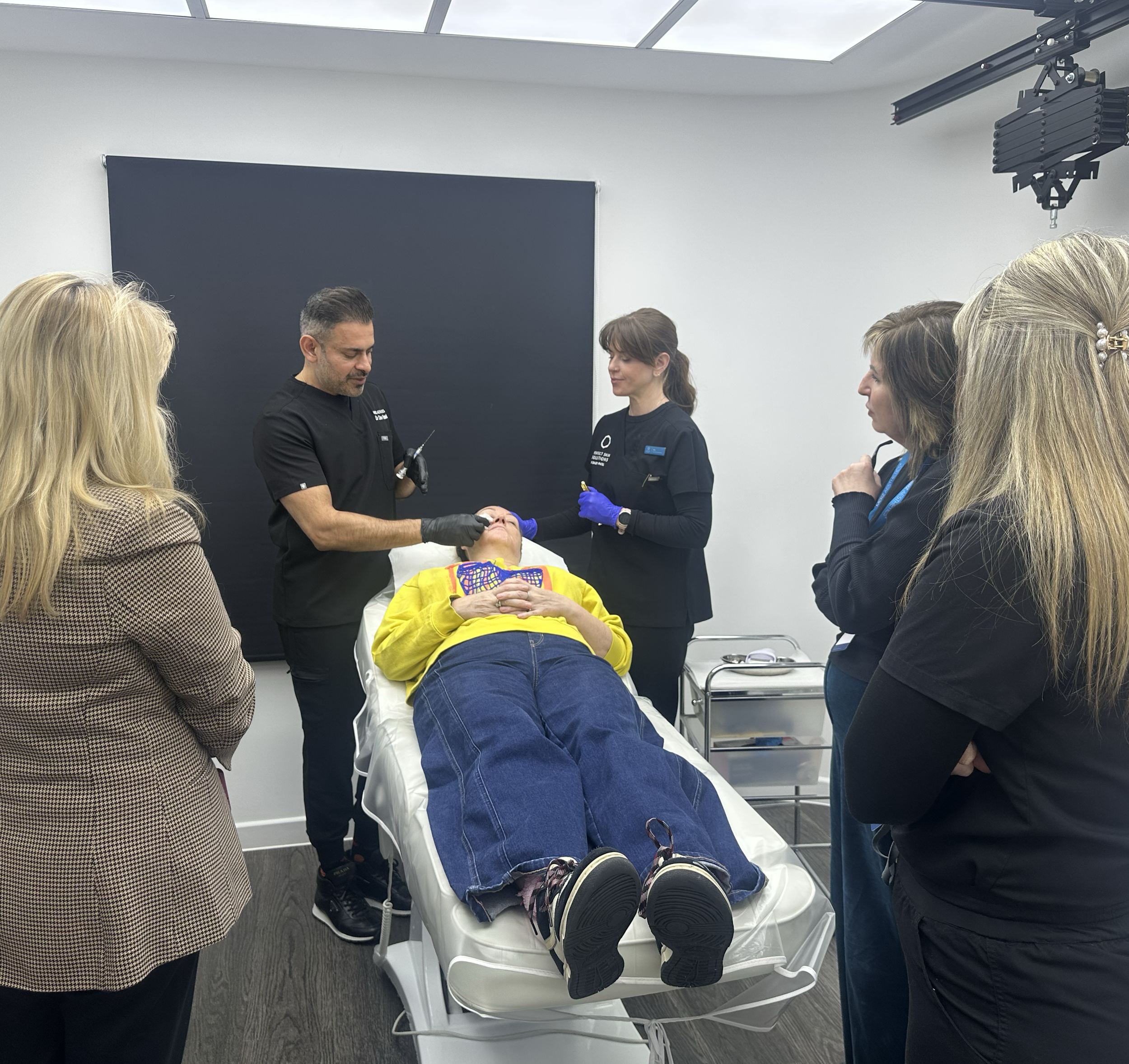 Medical professionals and family members surrounding a woman lying on a hospital bed, receiving treatment or assessment in a clinical setting.