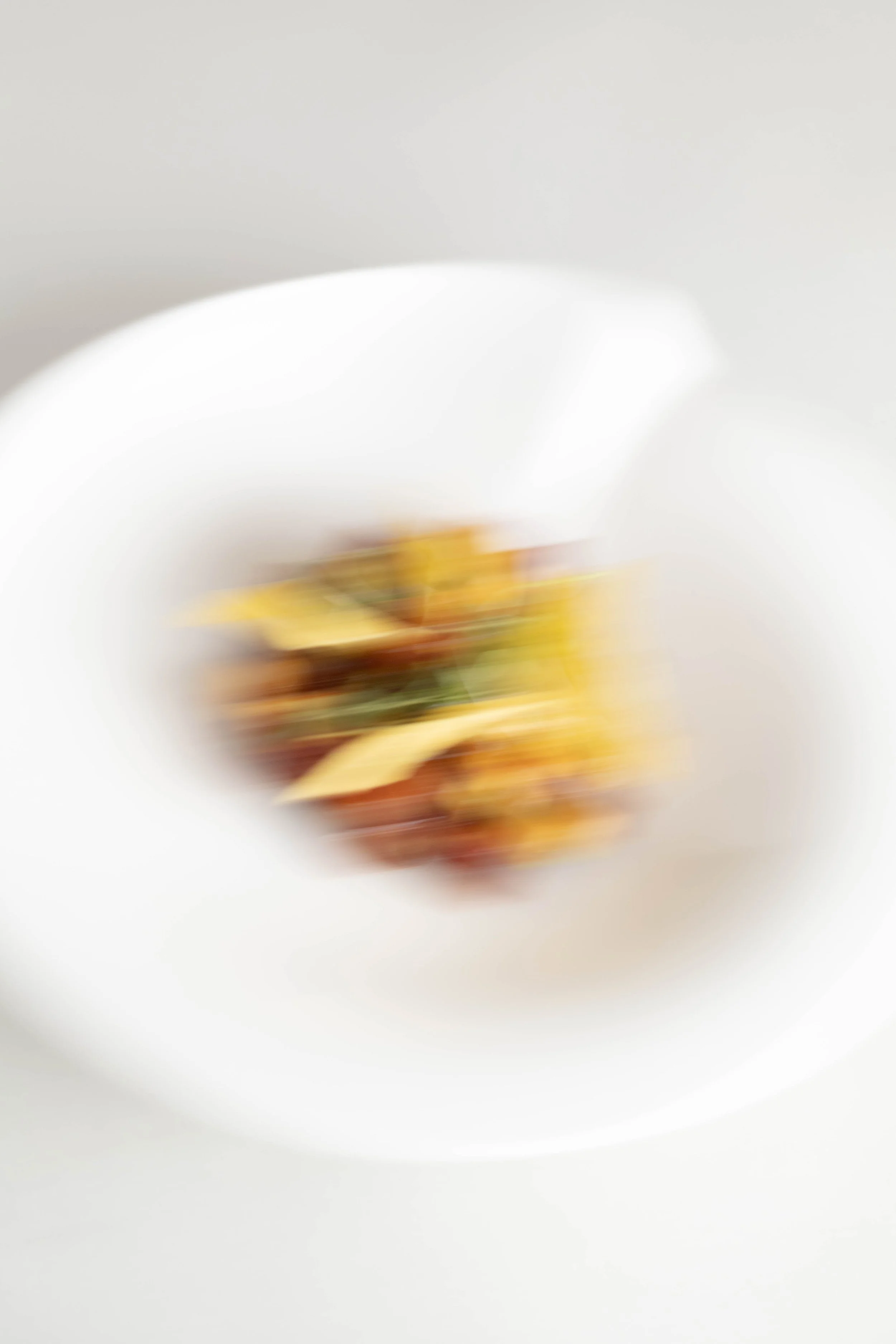 A white bowl with a blurred view of pasta in the center, with a light-colored background.