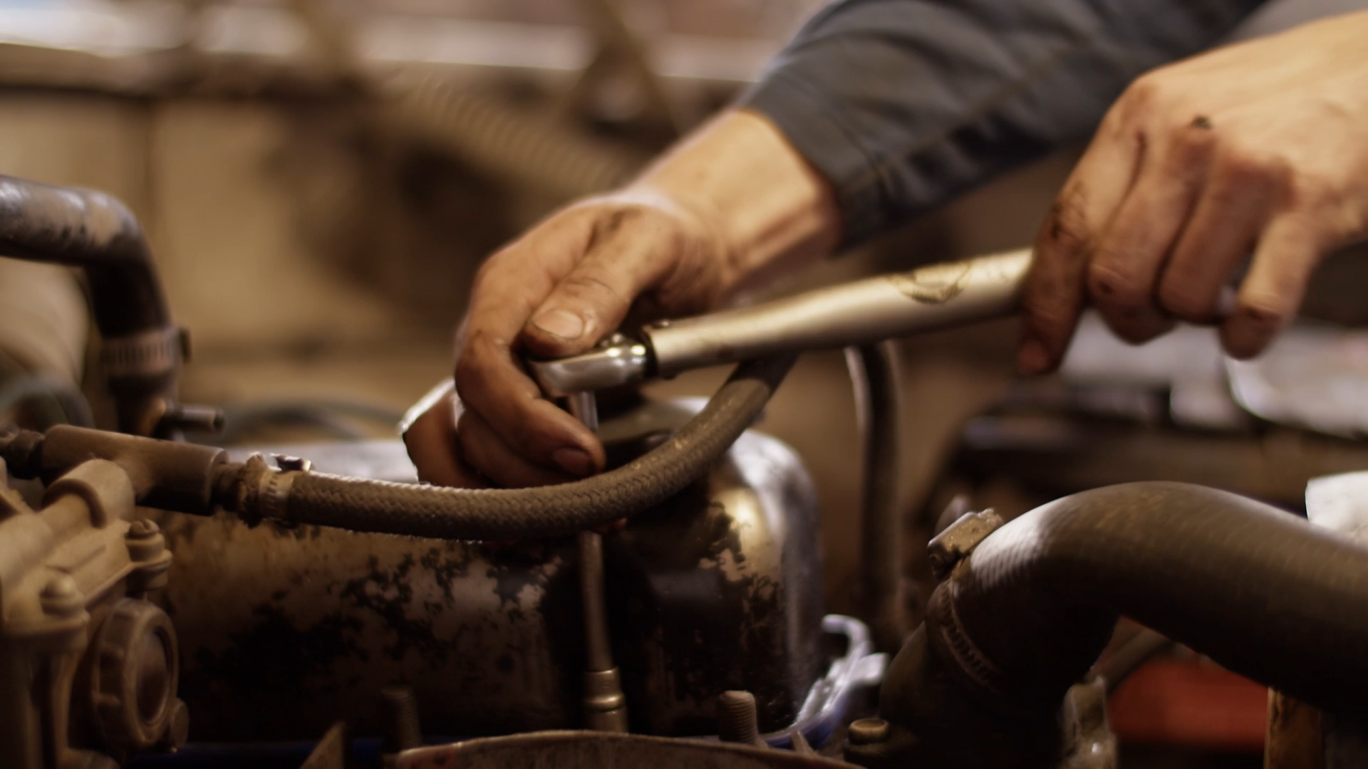 A mechanic's dirty hands working on a car engine, adjusting a metal component in a close-up shot.