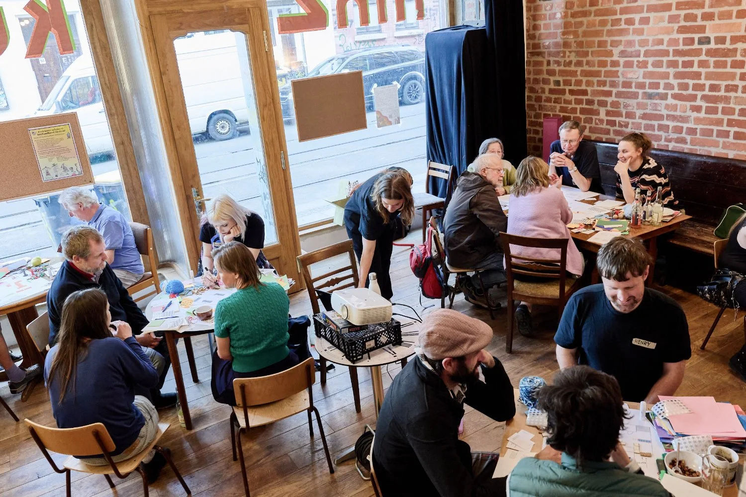 Mixed groups of four and five people sit around tables with diy materials