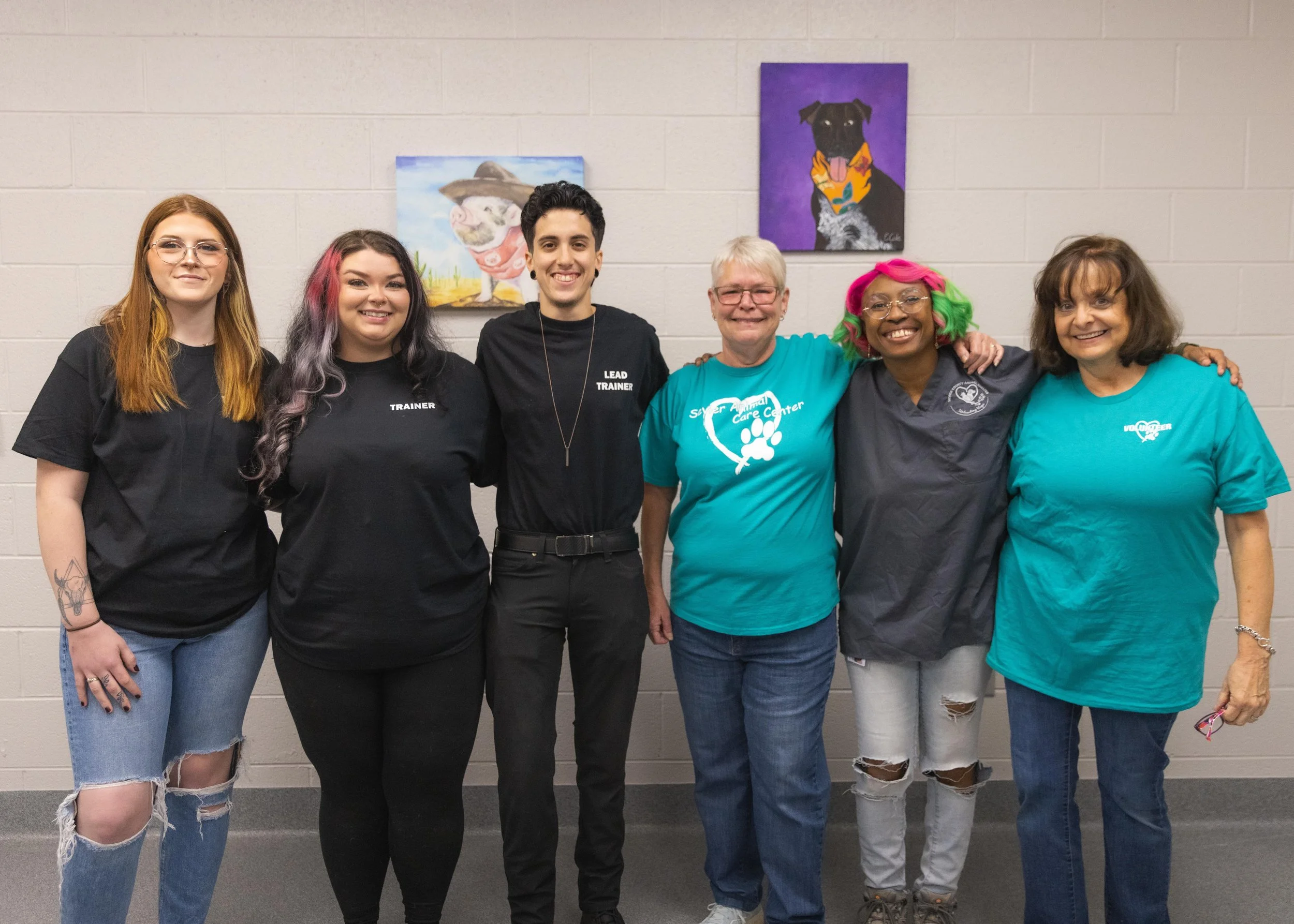 A group of people taking a picture in front of a wall with paintings of animals | Sevier County Animal Shelter