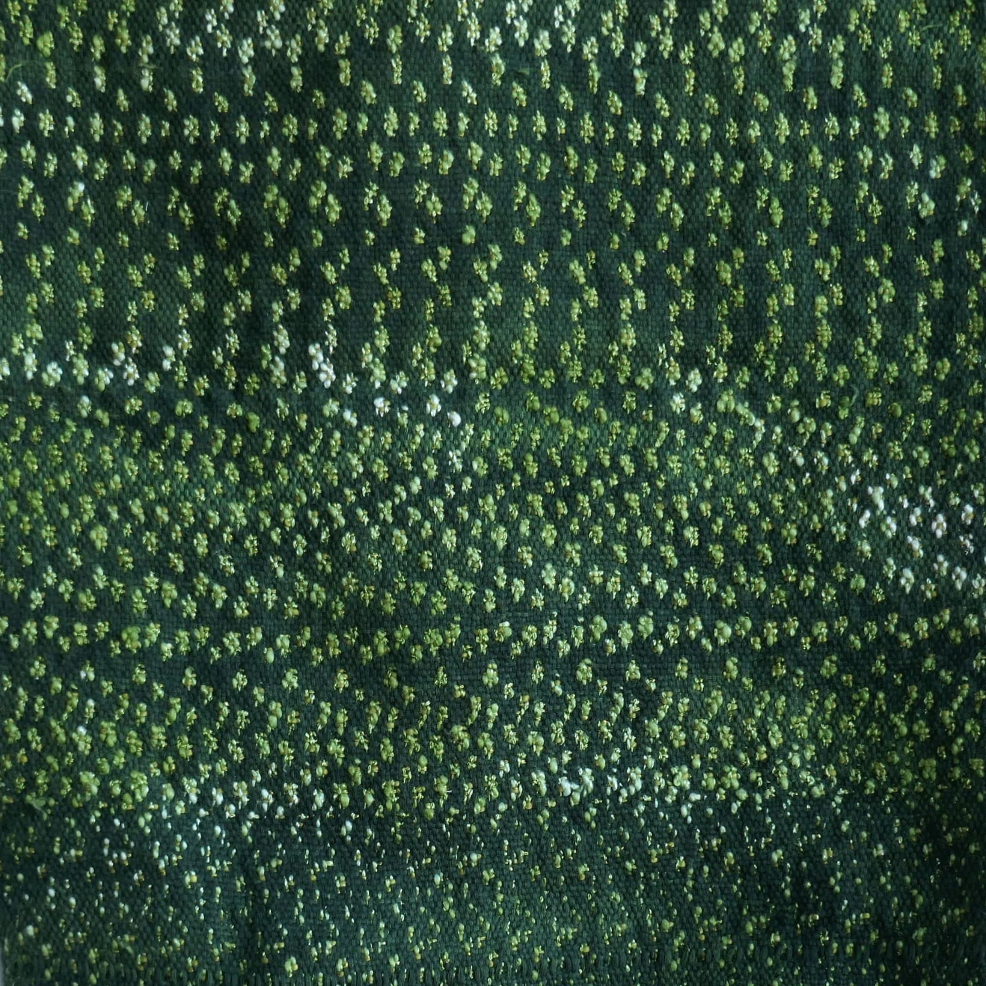 Nahaufnahme eines gewebten Stoffmusters mit kleinen blumenartigen Formen in dunklem und hellem Grün.