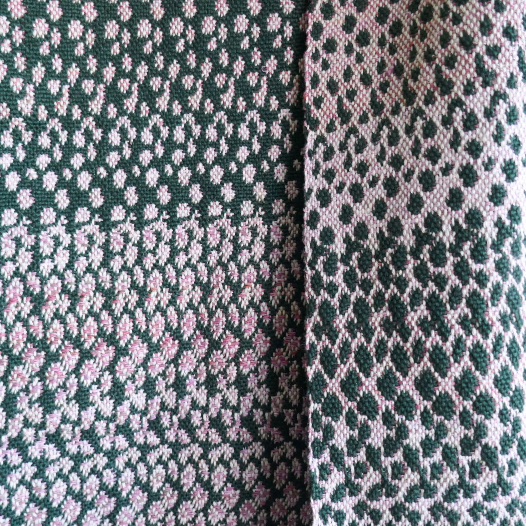 Nahaufnahme eines farbenfrohen gewebten Stoffes mit einem blattartigen Muster in Rosa, Weiß und Dunkelgrün.
