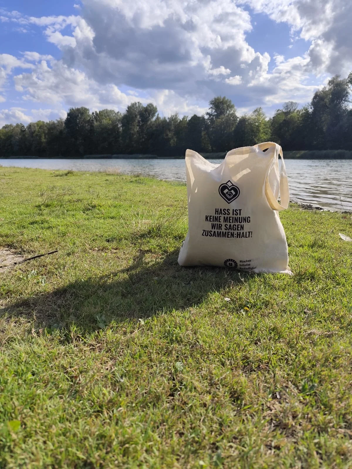 Foto von einem Stoffbeutel mit einem print. Der beutel liegt auf dem Boden und befindet sich in einen natürlichen umgebing am See