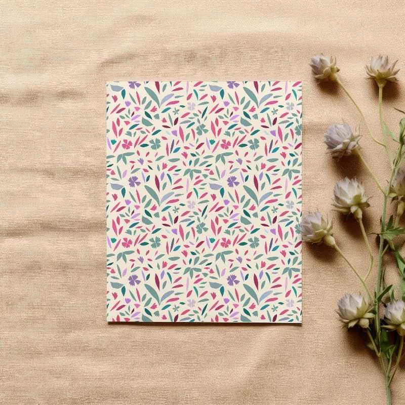 Papier mit buntem Blumenmuster neben weißen Blumen auf beigem Stoffhintergrund.