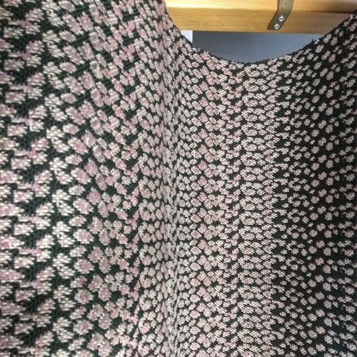 Nahaufnahme eines farbenfrohen gewebten Stoffes mit einem blattartigen Muster in Rosa, Weiß und Dunkelgrün.