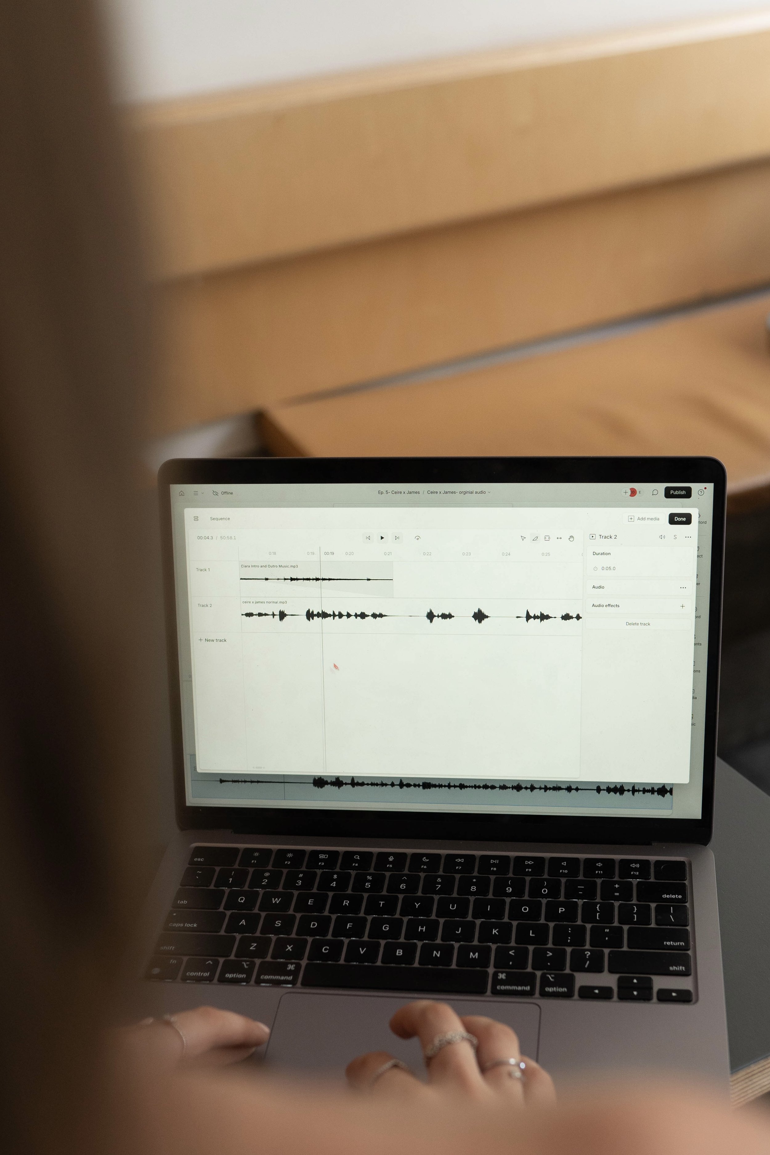 A person working on a laptop with audio editing software open on the screen.