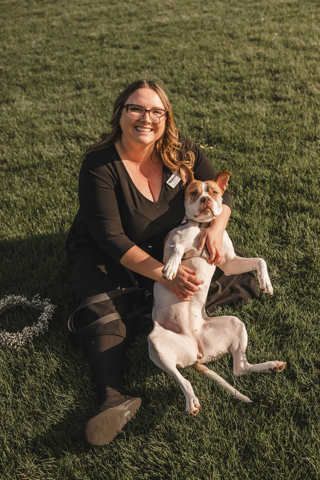 Wags of Love dog wedding attendant sitting in the grass giving belly rubs to dog during wedding.