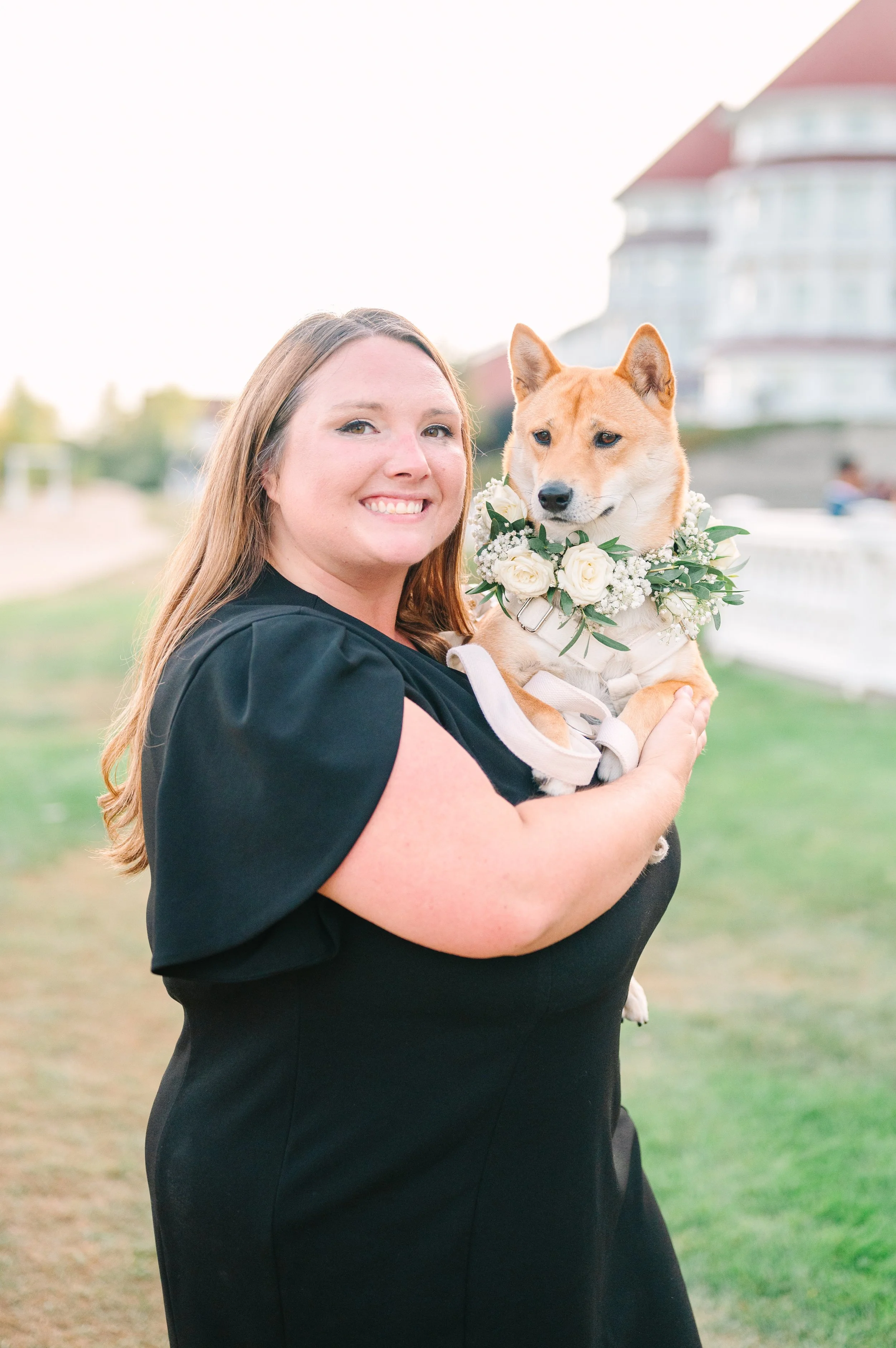 Professional wedding dog attendant holding dog with wedding floral collar.  