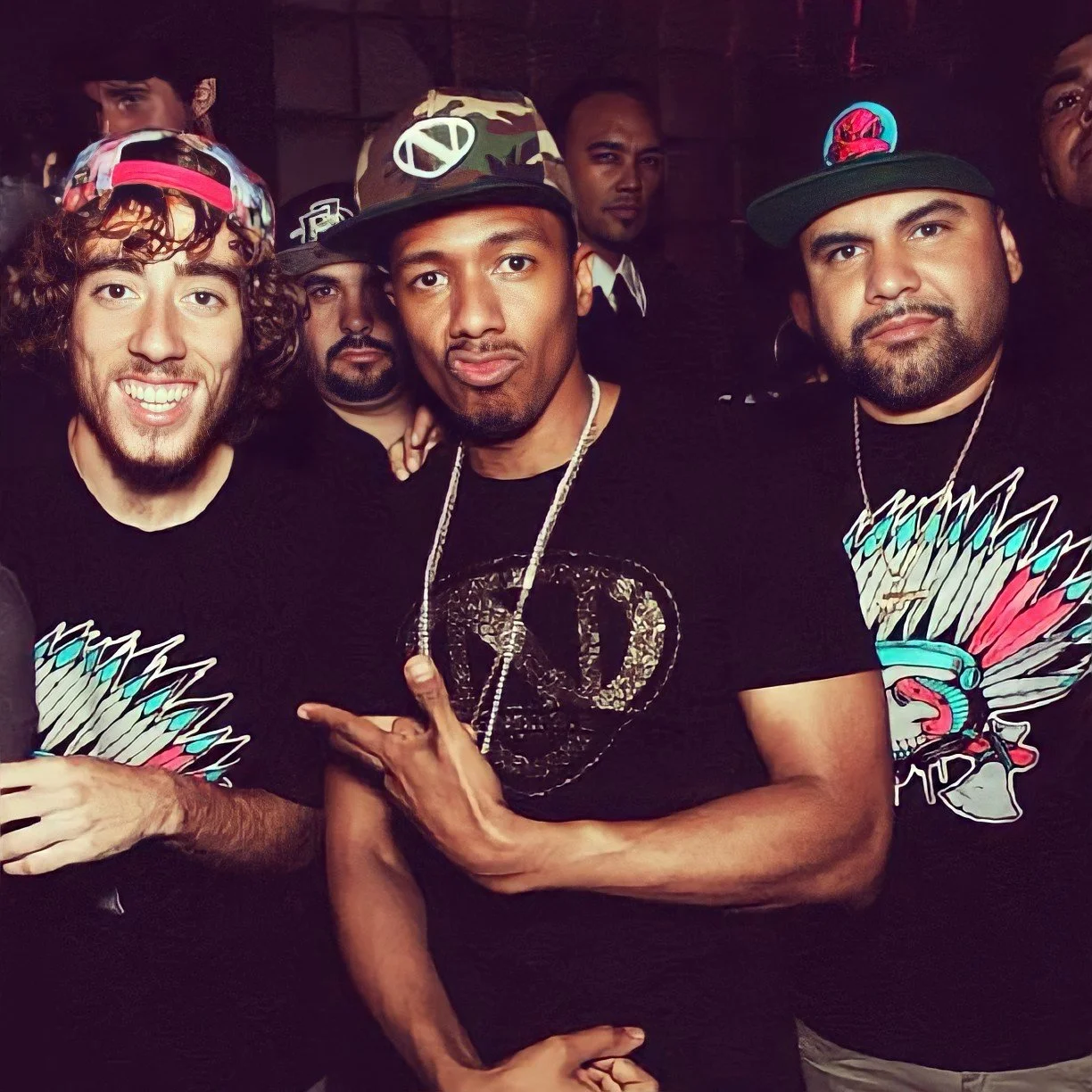 A group of five men posing together at a social event, wearing casual clothes and hats, with some smiling and making hand gestures.