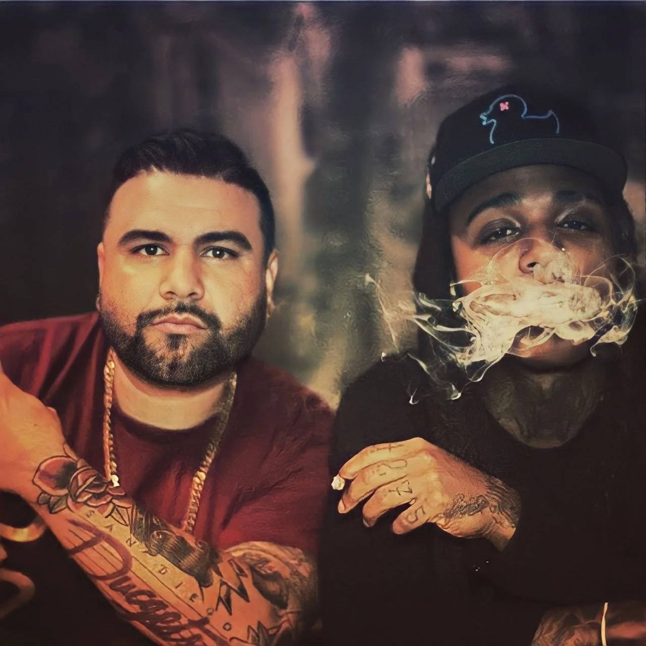 A digitally enhanced image featuring two men with tattoos and jewelry. The man on the left has a beard, short dark hair, a gold chain, and tattoos on his arm. The man on the right has a cap, tattoos on his hand, and is exhaling smoke or vapor, creati