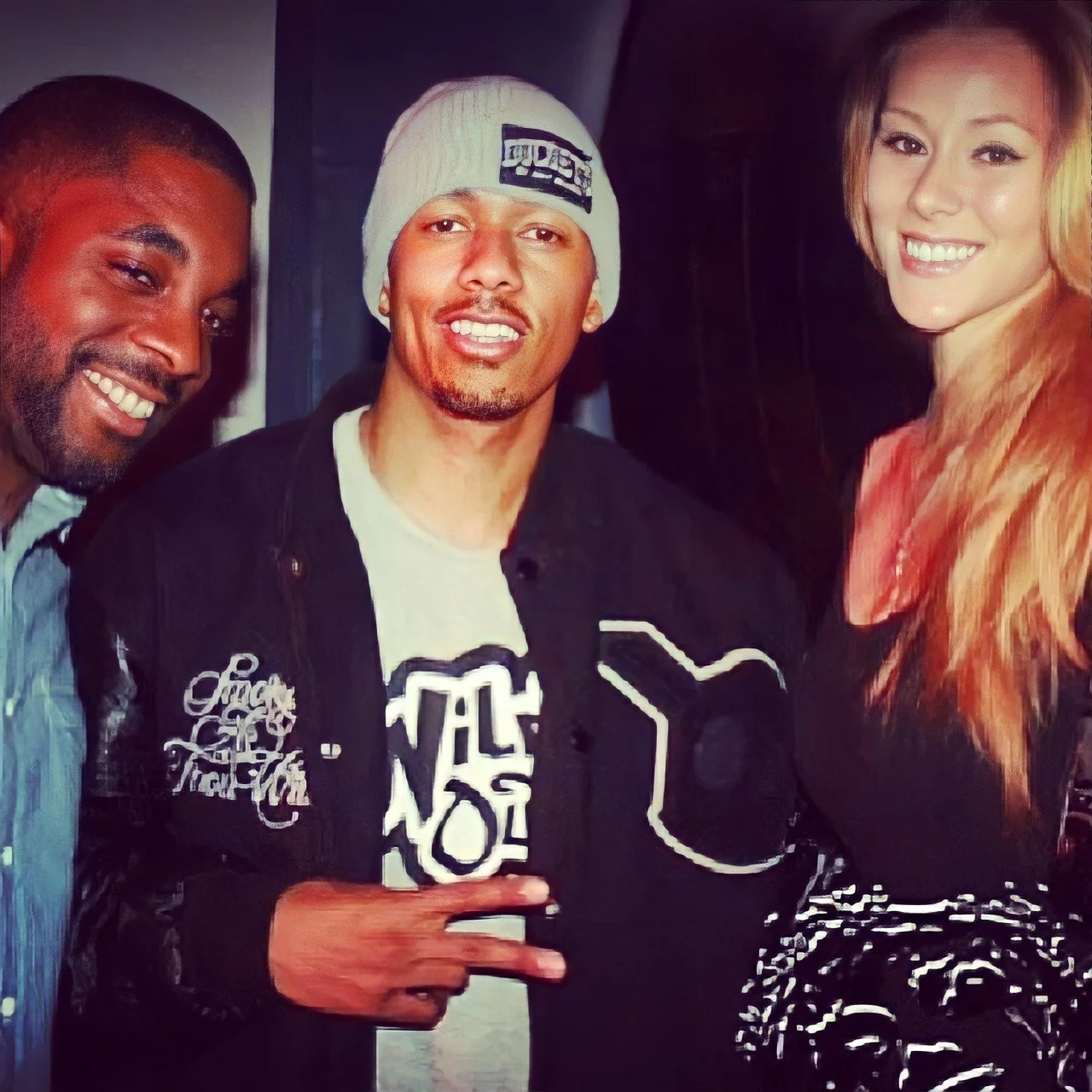 Group of three young adults smiling, standing close together, with one giving a peace sign, in a casual indoor setting.