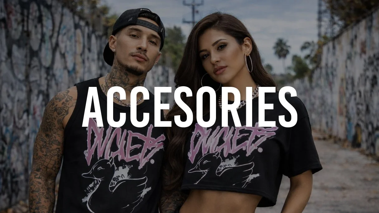 Two young adults, a man and a woman, standing in an urban alley covered in graffiti. They wear matching black graphic T-shirts, and the word 'ACCESSORIES' is overlaid on the image.