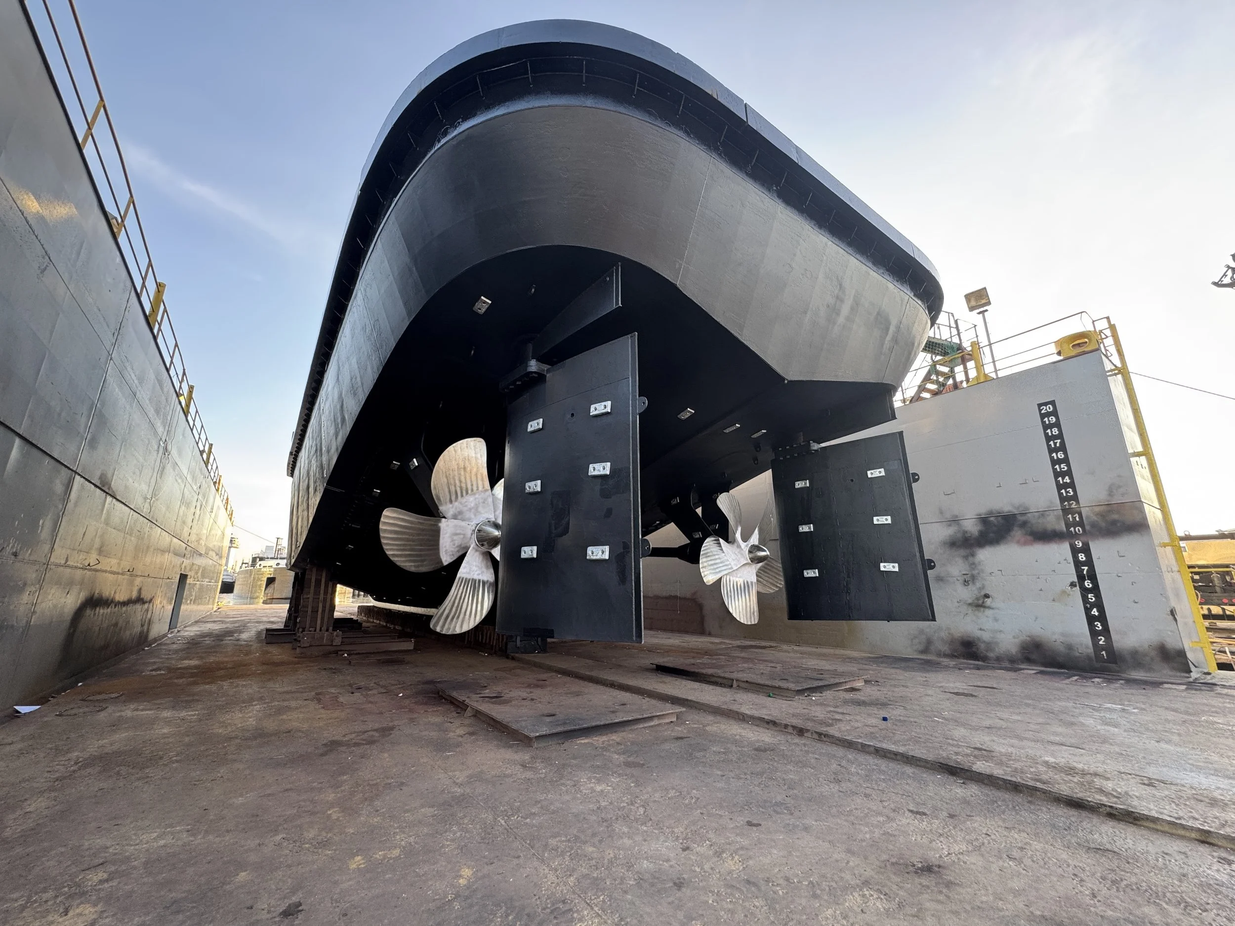 Large ship hull with twin propellers in a dry dock, viewed from below