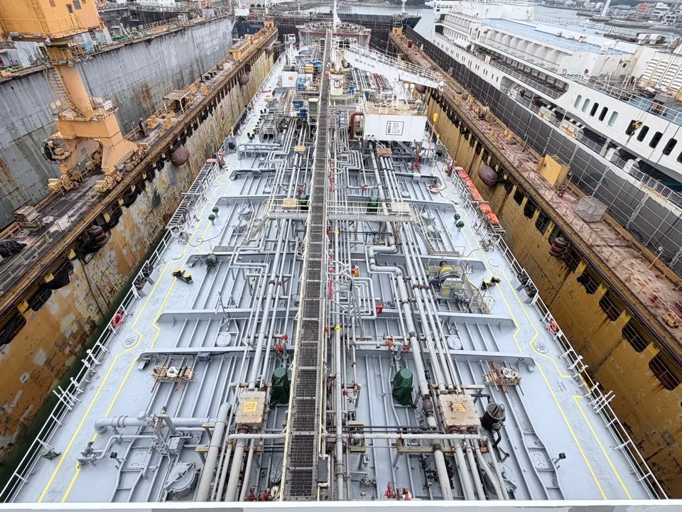 Aerial view of a ship under construction in a dry dock, showing its complex network of deck piping and equipment.