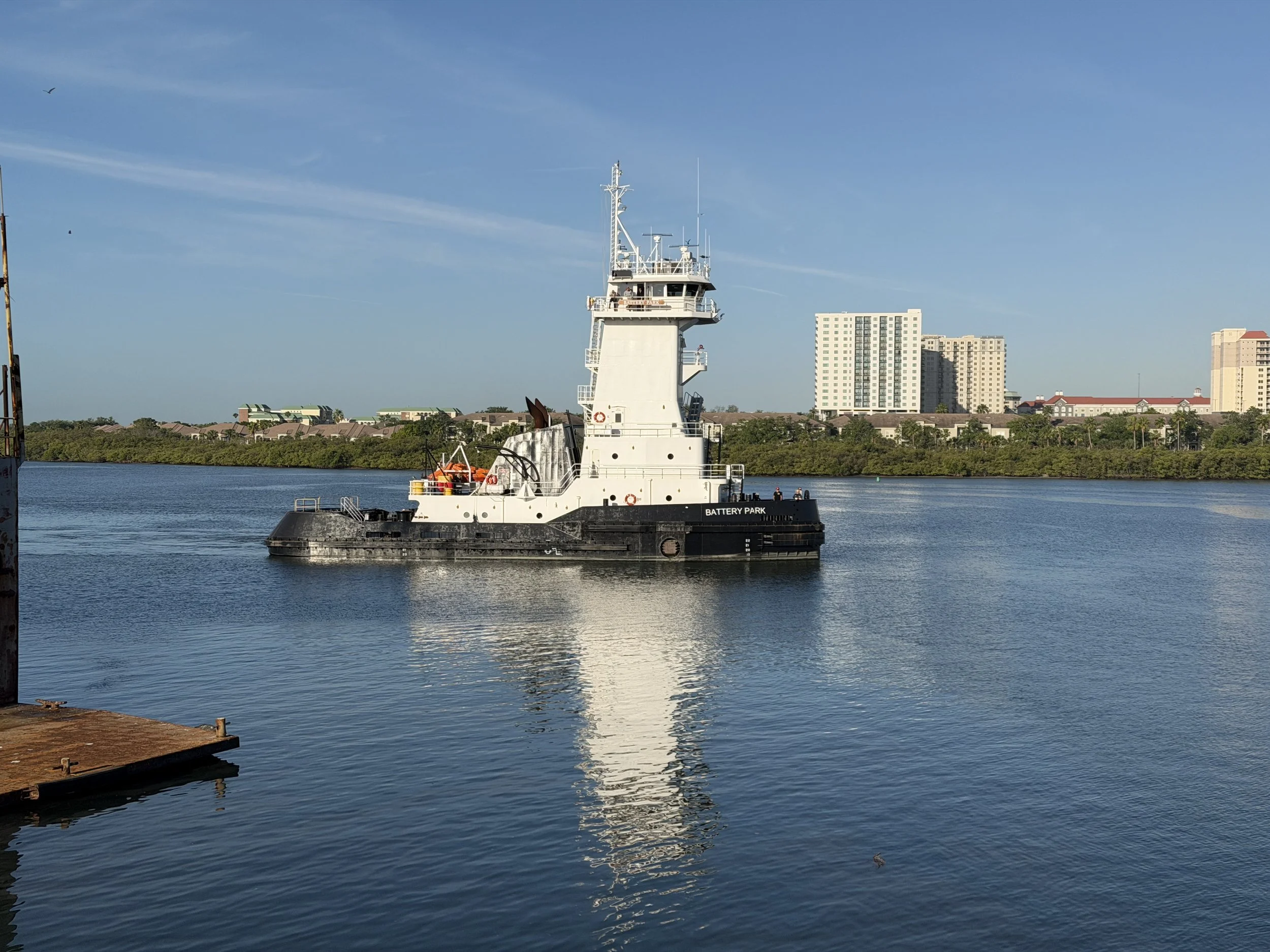Battery Park tugboat cruising on calm water with waterfront buildings in the background