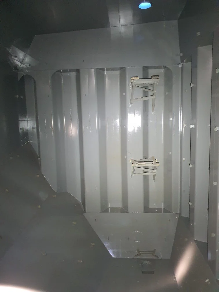 Empty gray industrial compartment with metal walls, fold-down brackets, and a floor hatch