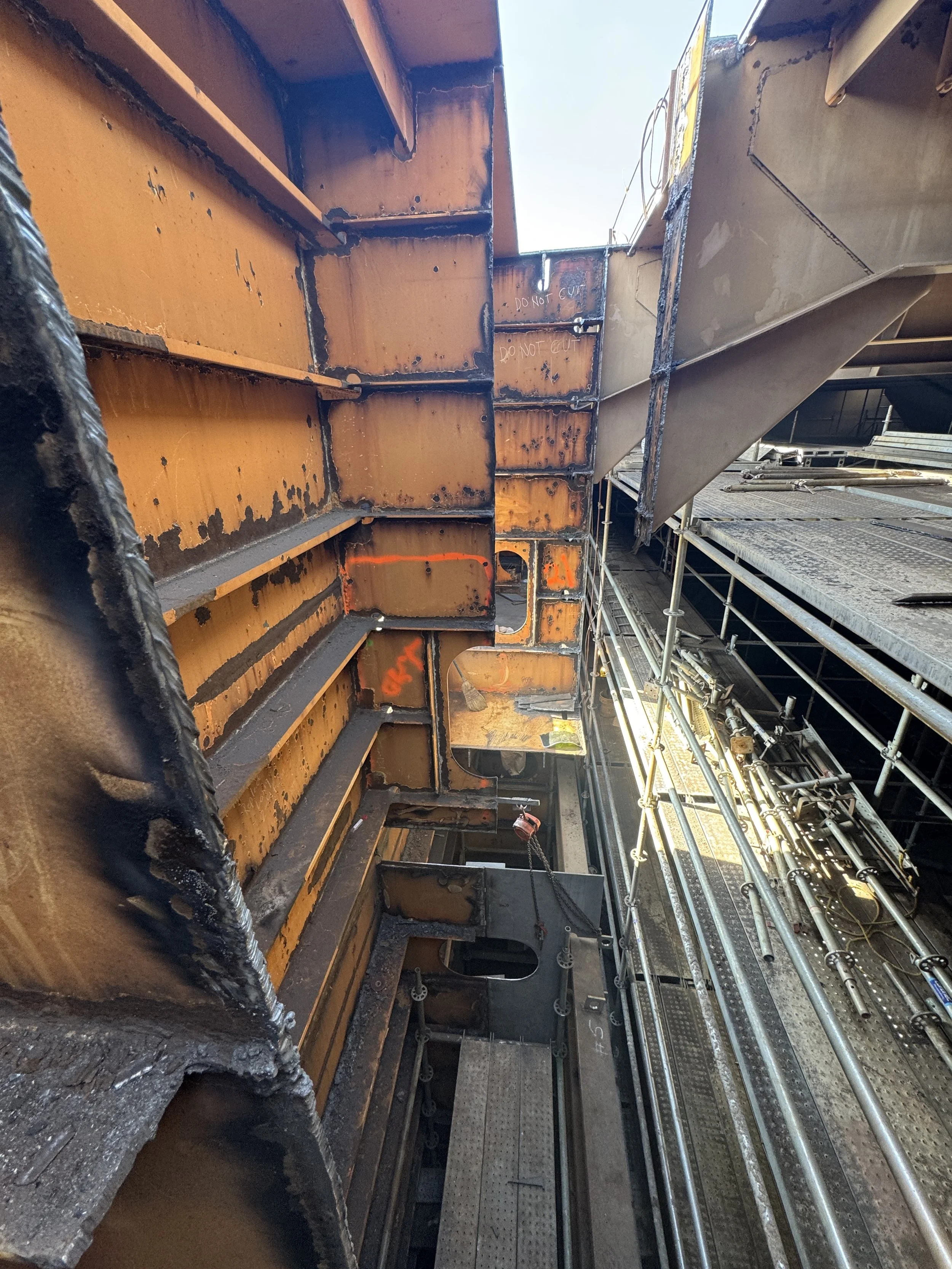 Industrial construction site with rusted steel beams, scaffolding, pipes, and elevated metal walkways.