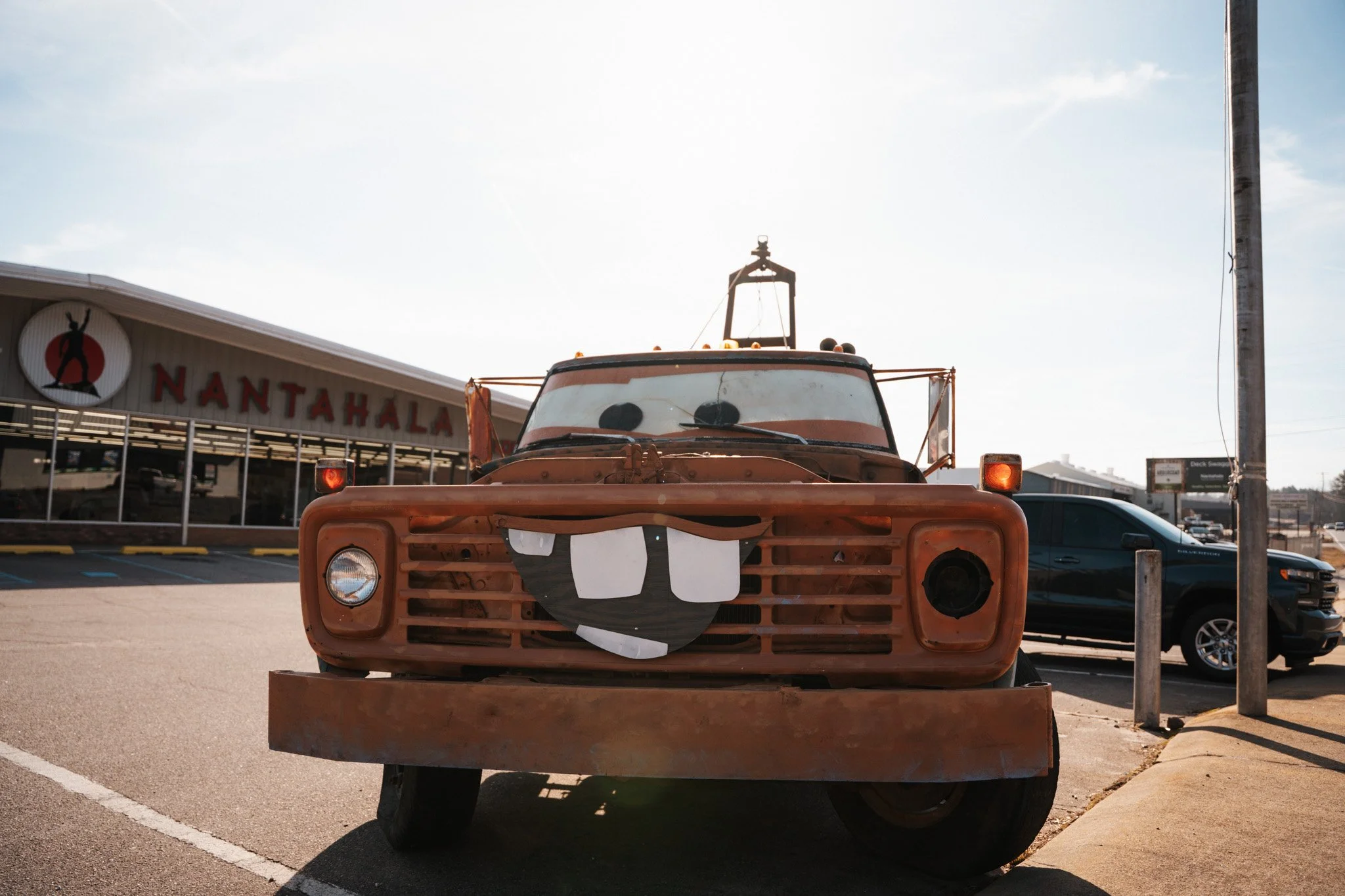 Rusty vehicle with cartoonish face, large tongue, and wide smile parked in a lot outside Nantahala store.