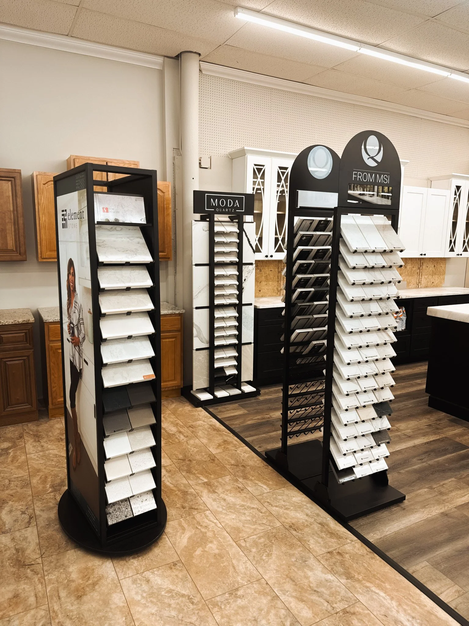 Display of marble and stone countertop samples in a home improvement store, with sample boards and cabinets in the background.