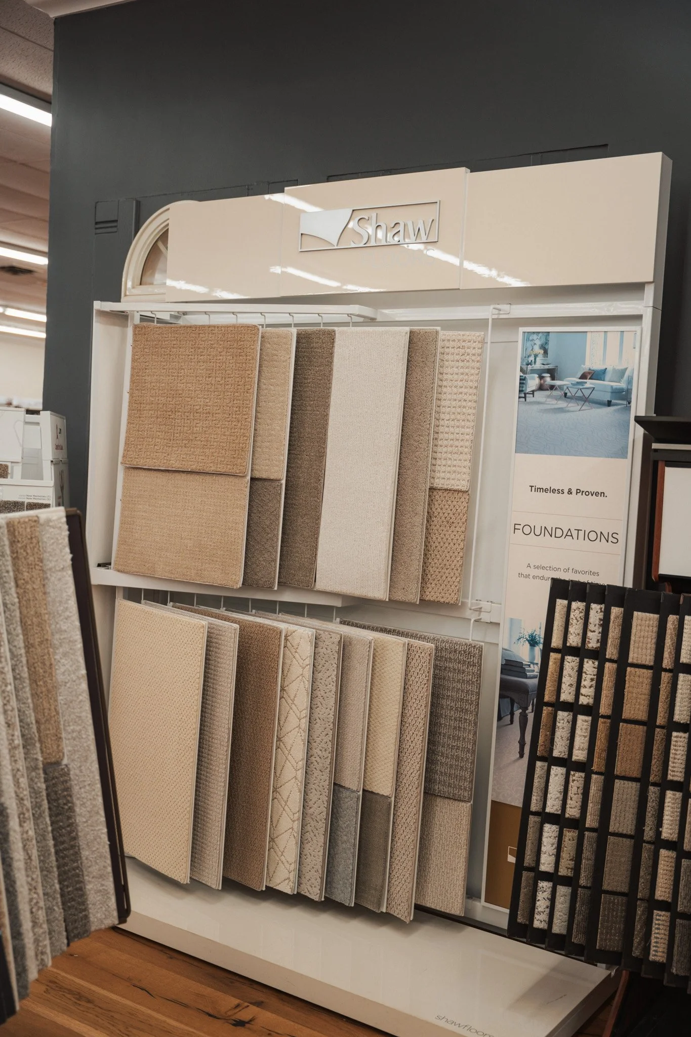 Display of various carpet sample swatches on a stand at a flooring store, with a Shaw logo at the top.