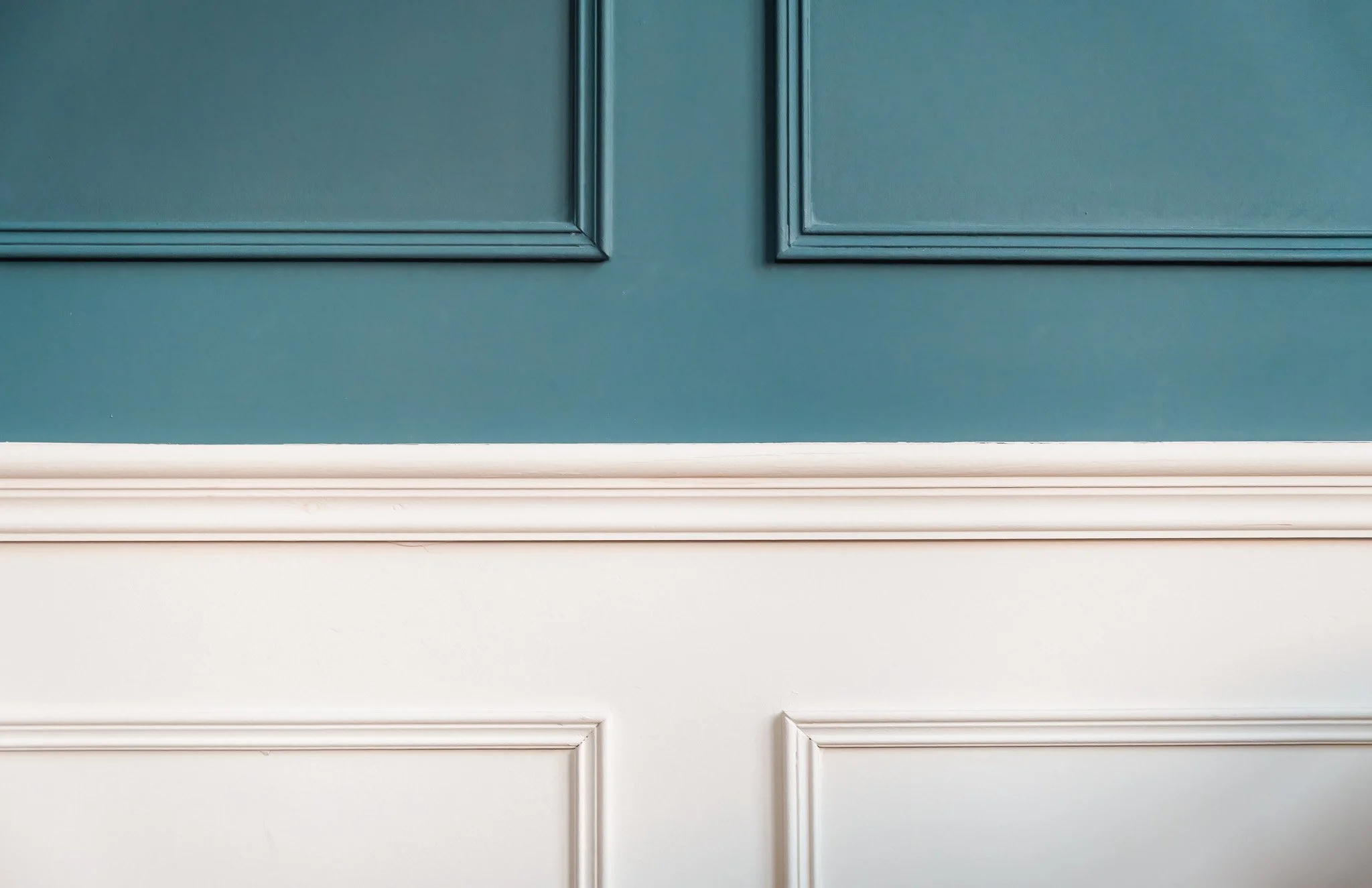 Close-up of a teal-colored cabinet door with decorative molding, above a white wainscoting and baseboard.